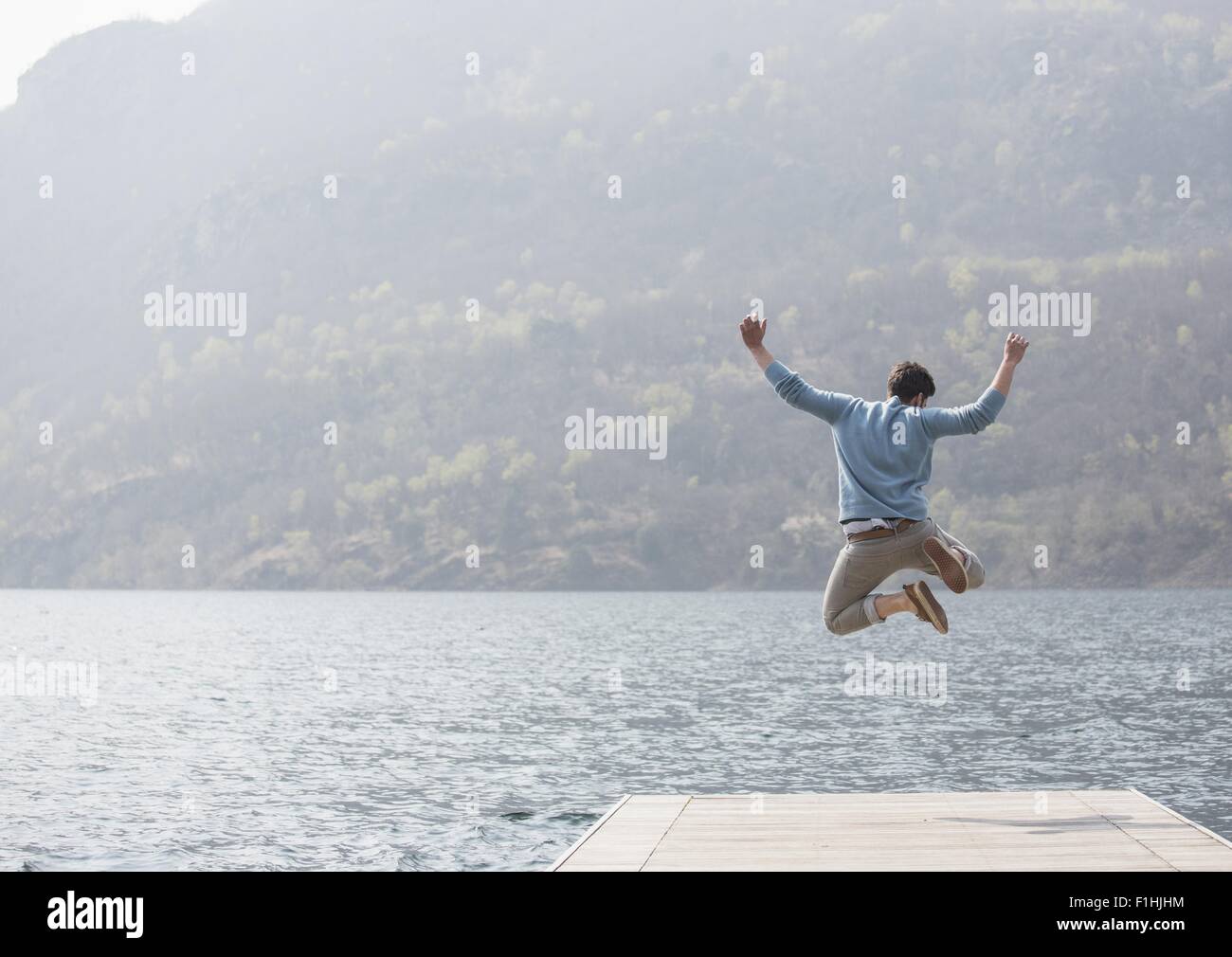 Rückansicht des jungen Mann springt auf Pier, Mergozzo See, Verbania, Piemont, Italien Stockfoto