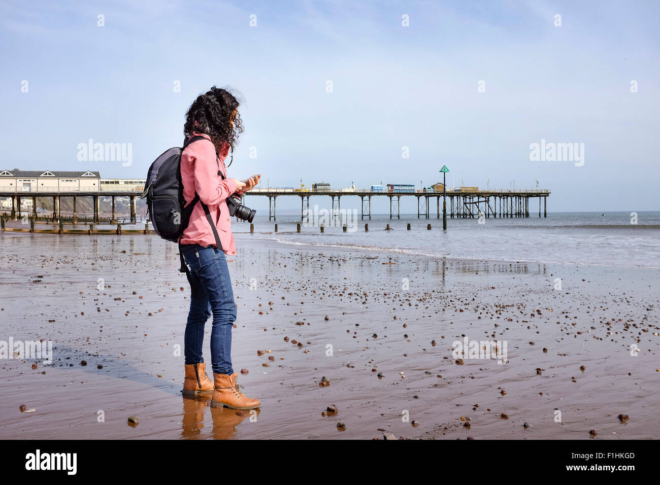 Einsame kaukasischen Brünette Reisende Frau mittleren Alters mit ihrem Handy am Strand in der Nähe von einem pier Stockfoto