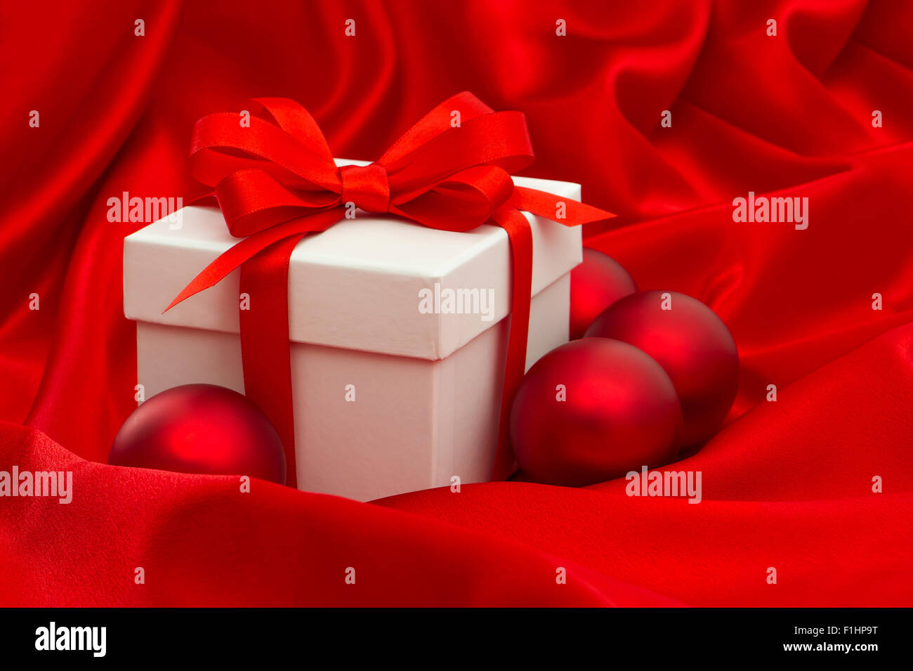 Weißen Geschenkbox mit Weihnachtsdekoration Kugeln über rote Seide Hintergrund Stockfoto