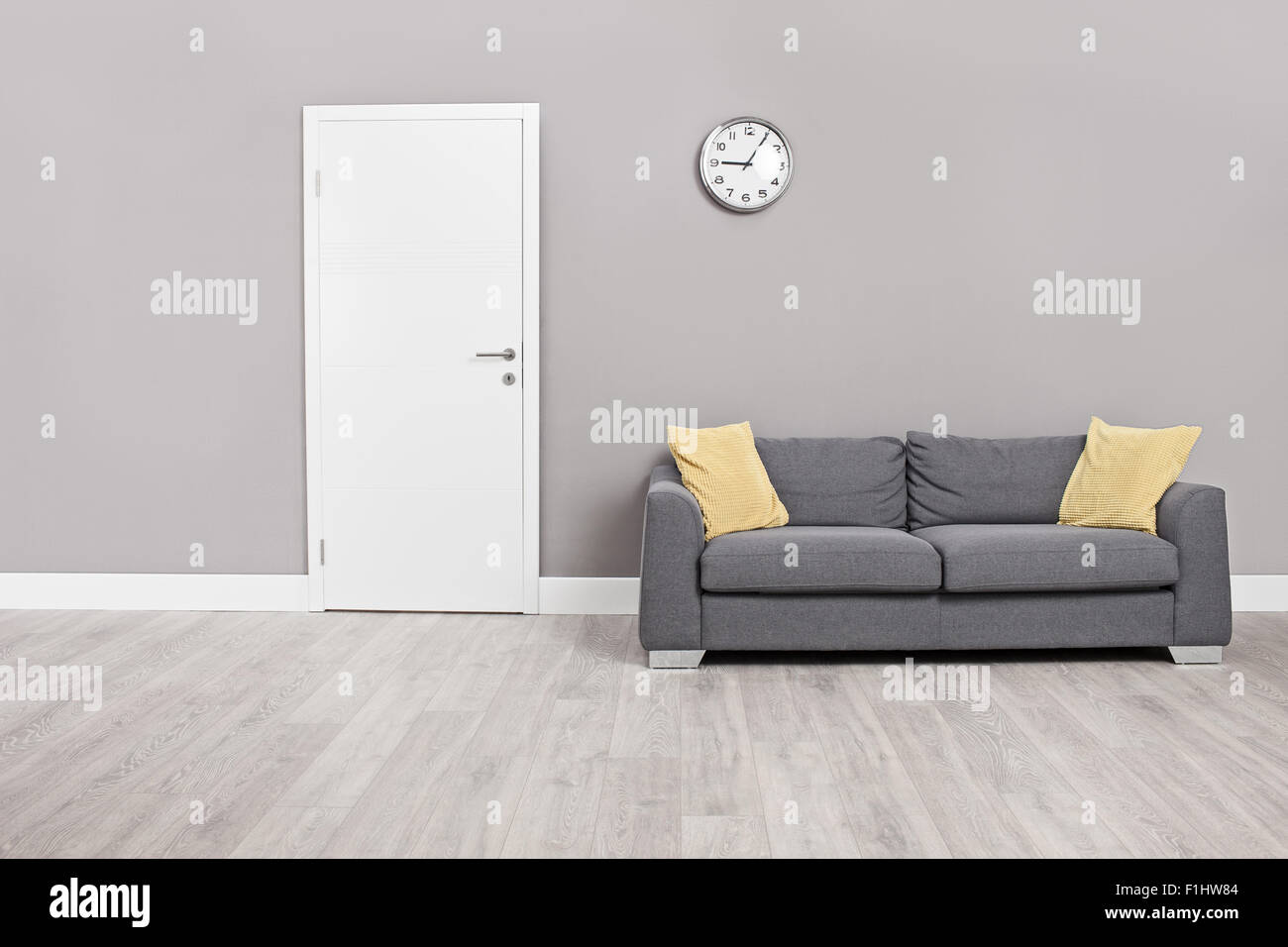 Leeres Wartezimmer mit einem modernen grauen Sofa vor der Tür und eine Uhr an der Wand Stockfoto