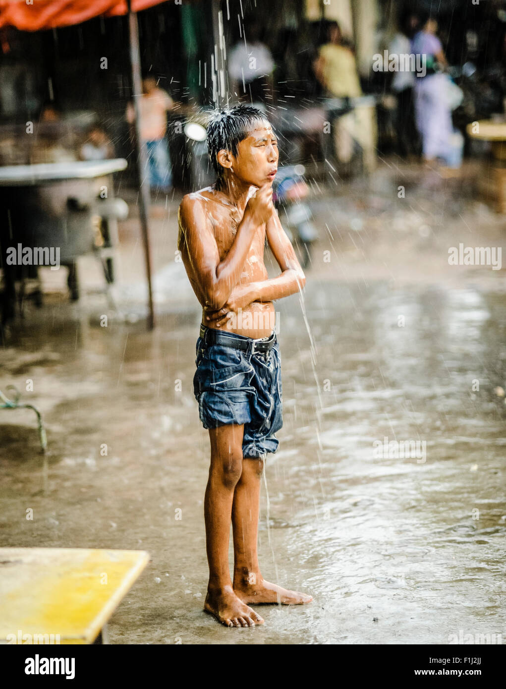 Burmesische junge nimmt Dusche im Regen tropft aus einer Plane Stockfoto
