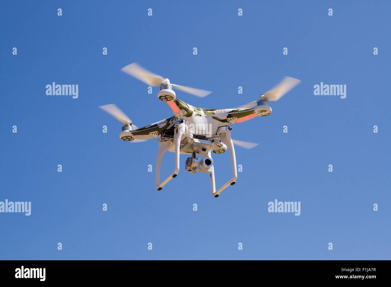 Camouflage Quadcopter, der mit einer Kamera vor einem blauen Himmel schwebt. Stockfoto
