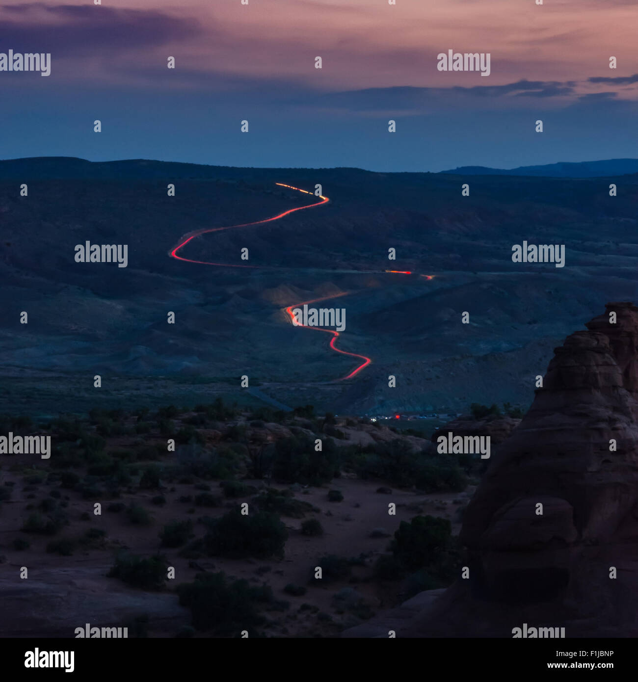 Wie Sonnenuntergang in die Nacht übergeht, ein Strom von Scheinwerfern wind durch den Arches National Park Stockfoto