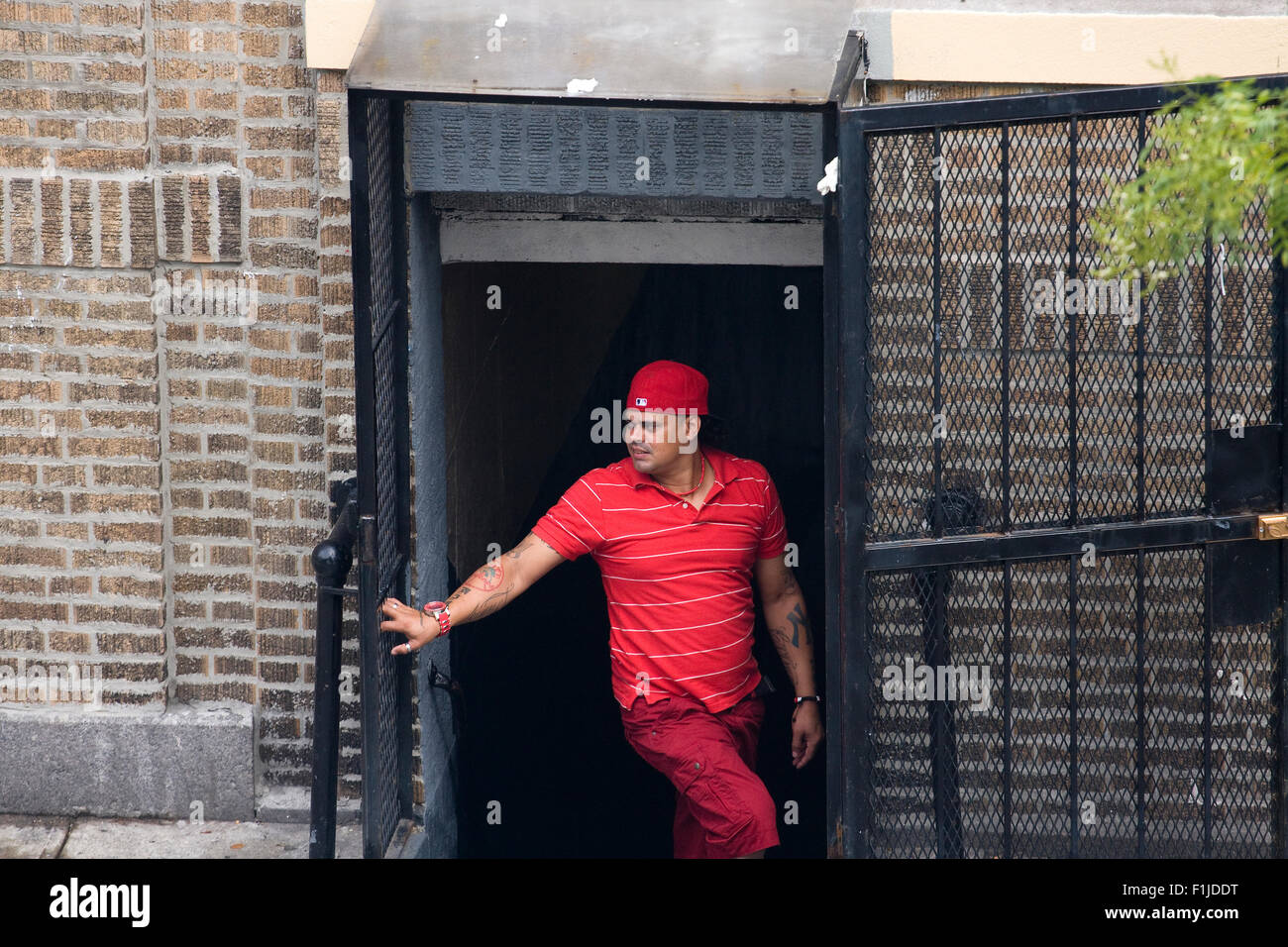 Hispanic Mitglied der Straßengang "Bloods" gekleidet in rot stehen heimlich in ein Zugangsstollen eines Mehrfamilienhauses. Stockfoto