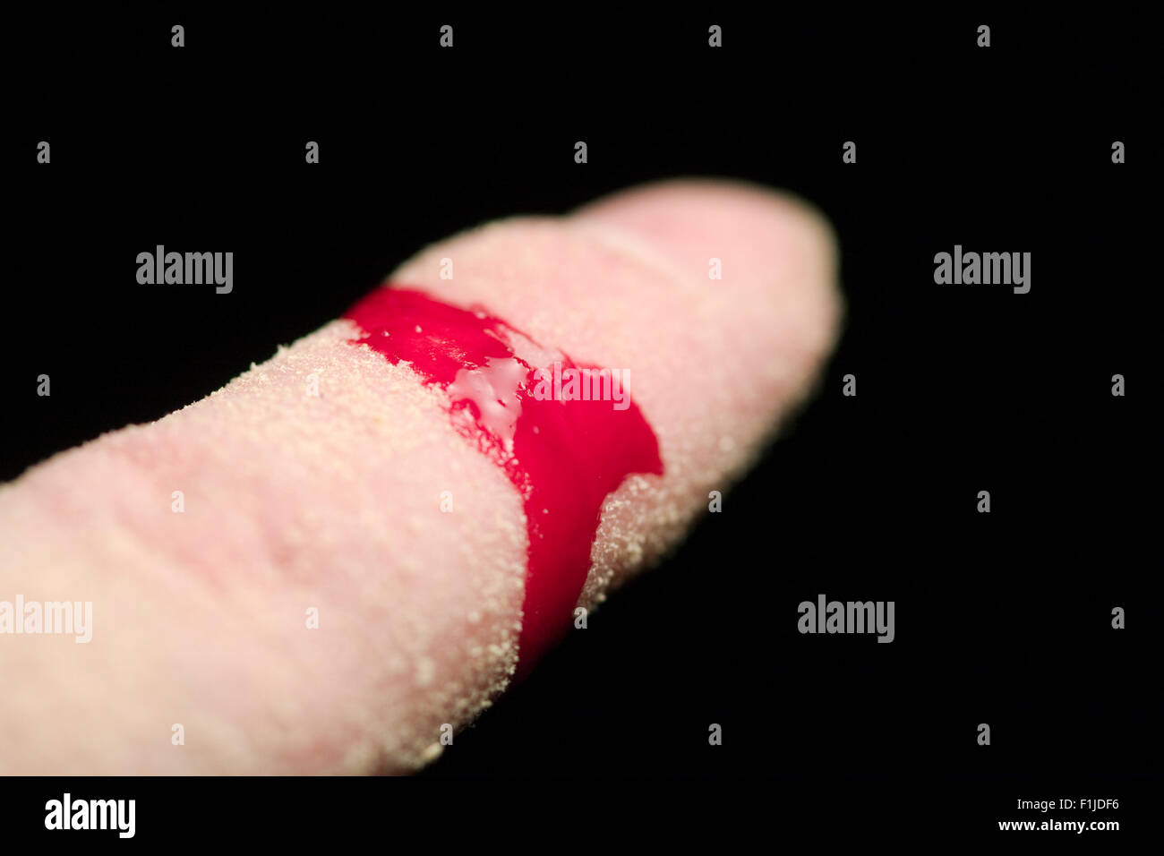 Ein Mann Zeigefinger mit Sägemehl bedeckt, während Blut aus einer Wunde auf schwarzem Hintergrund gestreamt wird Stockfoto