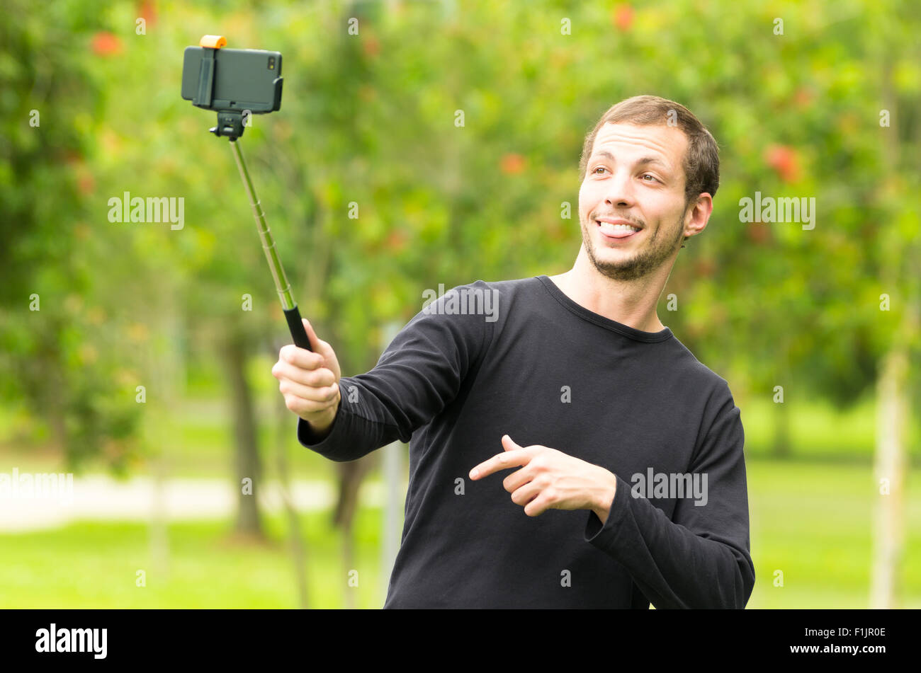 Hispanic Mann posiert mit Selfie Stick in Park Umgebung nehmen ein Foto von sich lächelnd Stockfoto