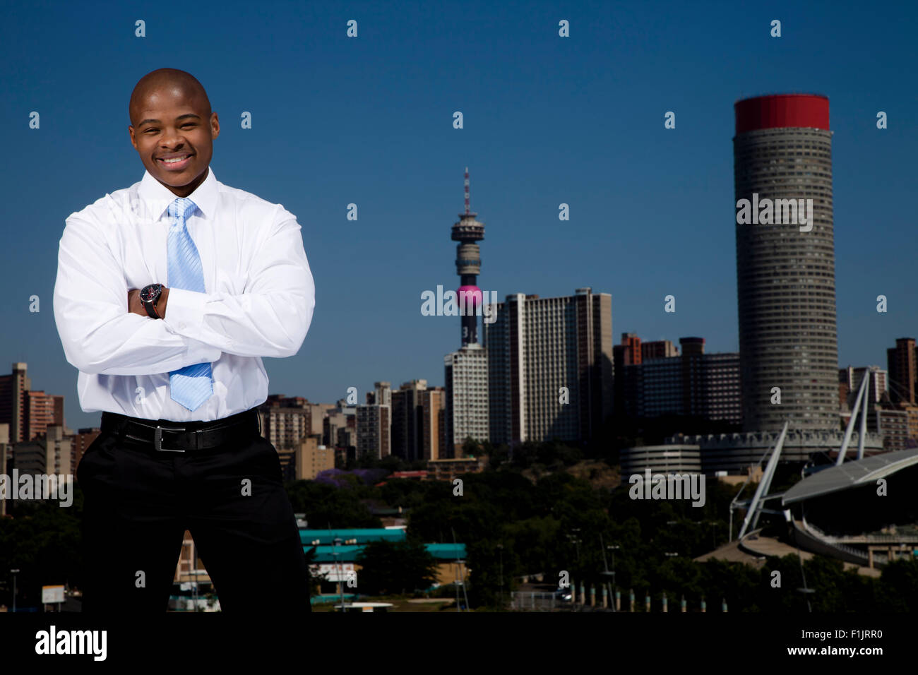 Elegant gekleidete Business-Mann stehend mit verschränkten mit Stadtbild im Hintergrund Stockfoto