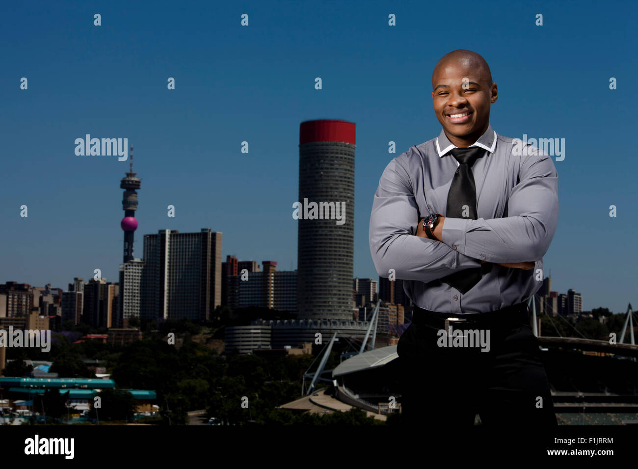Elegant gekleidete Business-Mann stehend mit verschränkten mit Stadtbild im Hintergrund Stockfoto