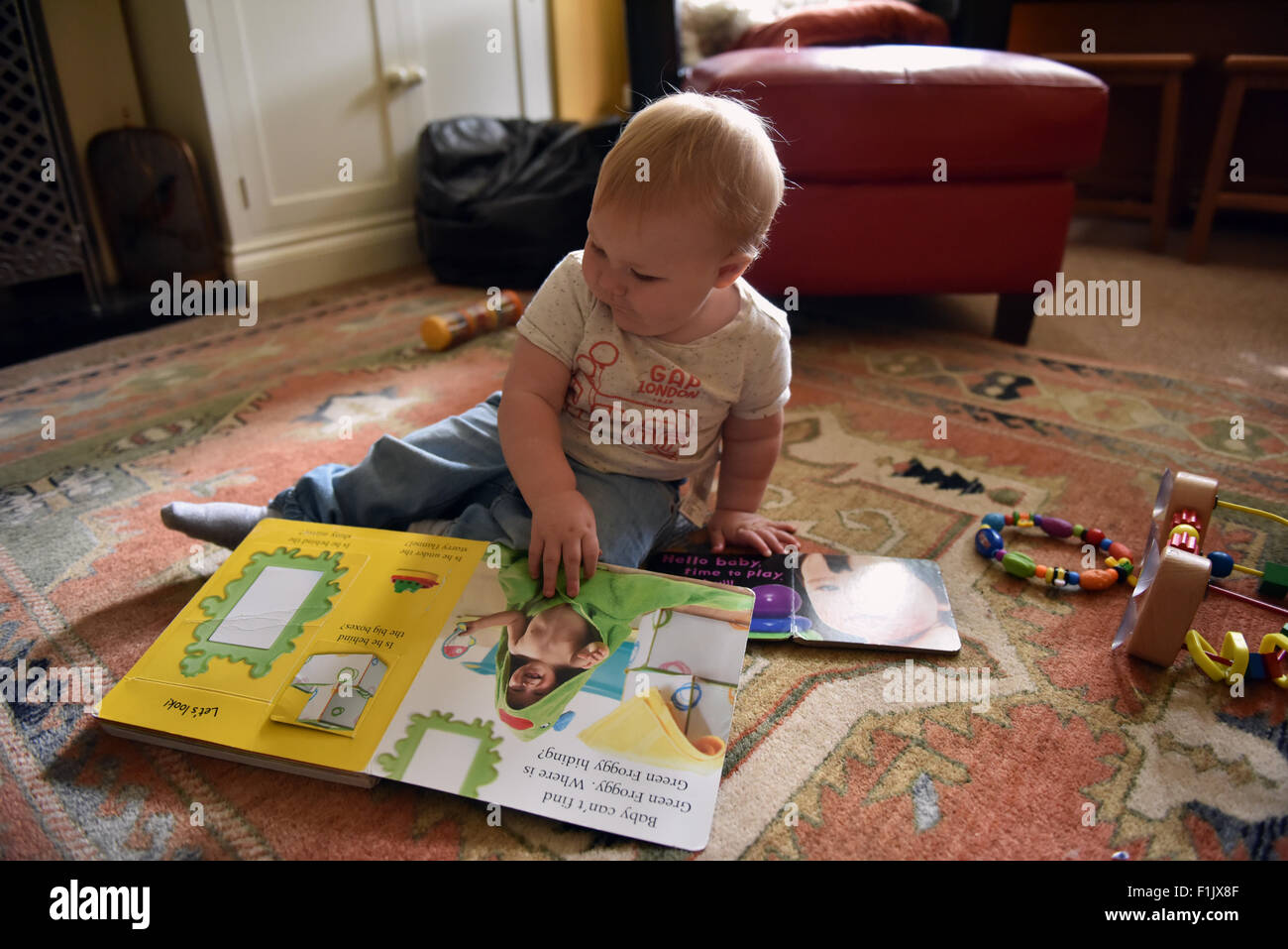 Einjähriges Kind Blick auf eine frühe Jahre Buch sitzt auf einem Teppich auf den Ausschnitt Segmenten ziehen unterschiedliche Sounds zu aktivieren Stockfoto