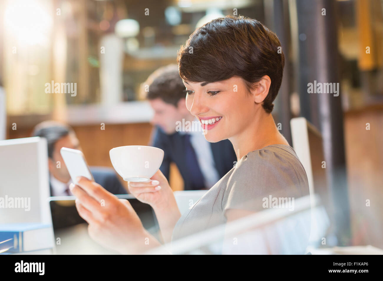 Geschäftsfrau, trinken Kaffee und SMS mit Handy im Büro Stockfoto