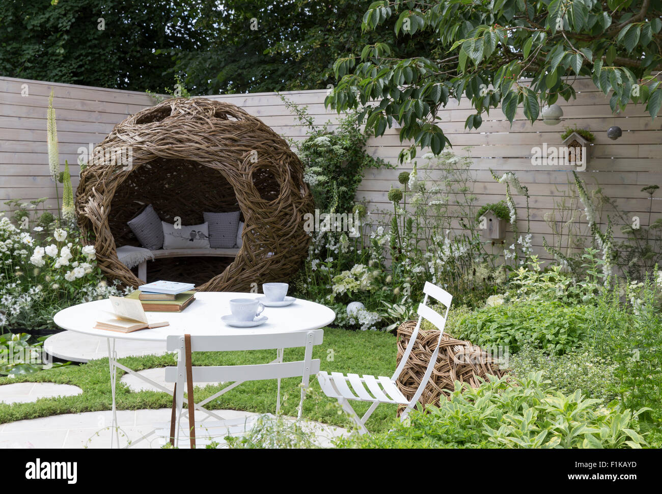 Eine kleine städtische Tierwelt Vogel freundlich Garten Kamille Rasen Schritt Steine und eine gewebte Weidenschote mit Bank und Kissen - weiße Blumen Sommer UK Stockfoto