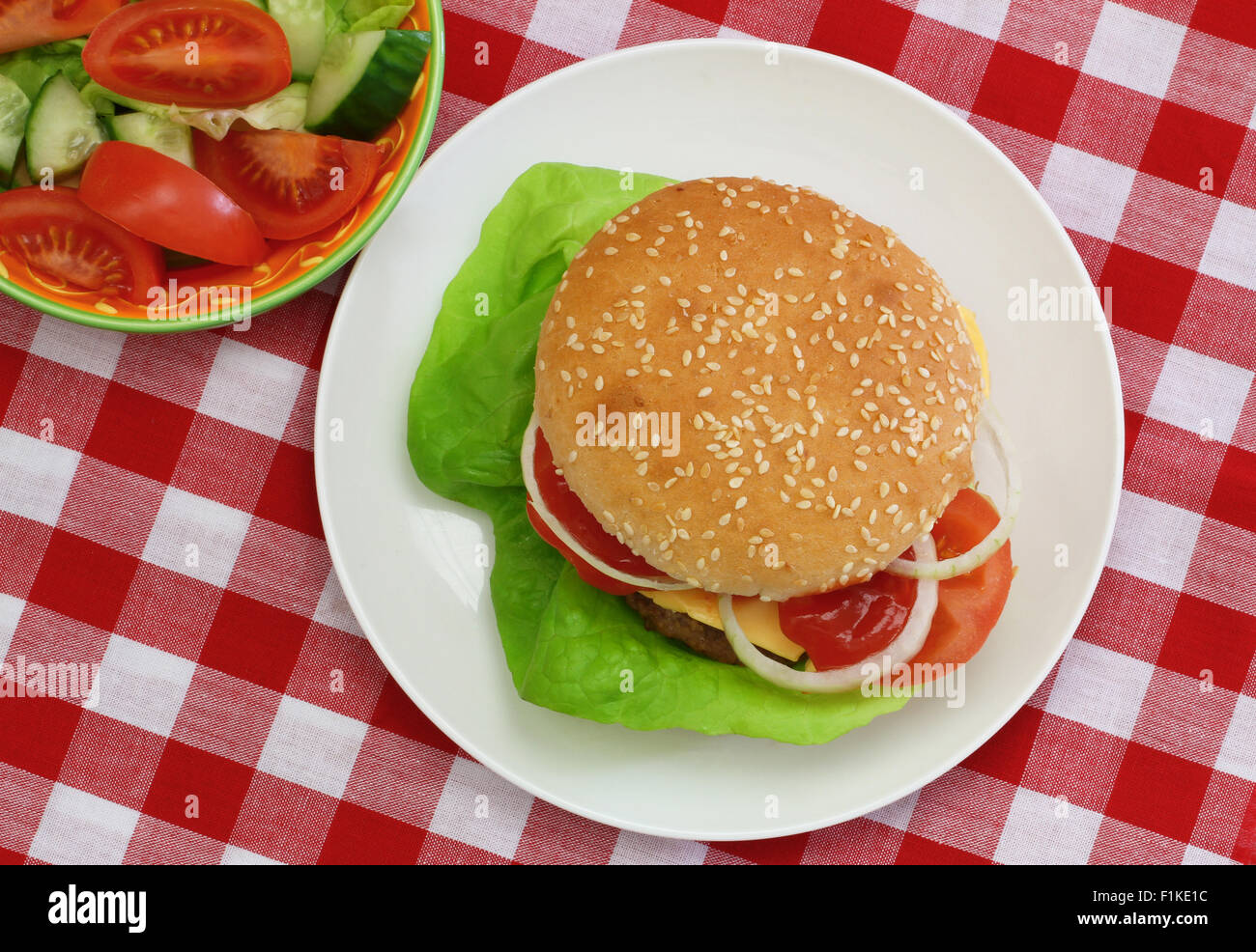 Cheeseburger mit grünem Salat, erschossen von der Spitze auf rot-weiß karierte Tuch Stockfoto