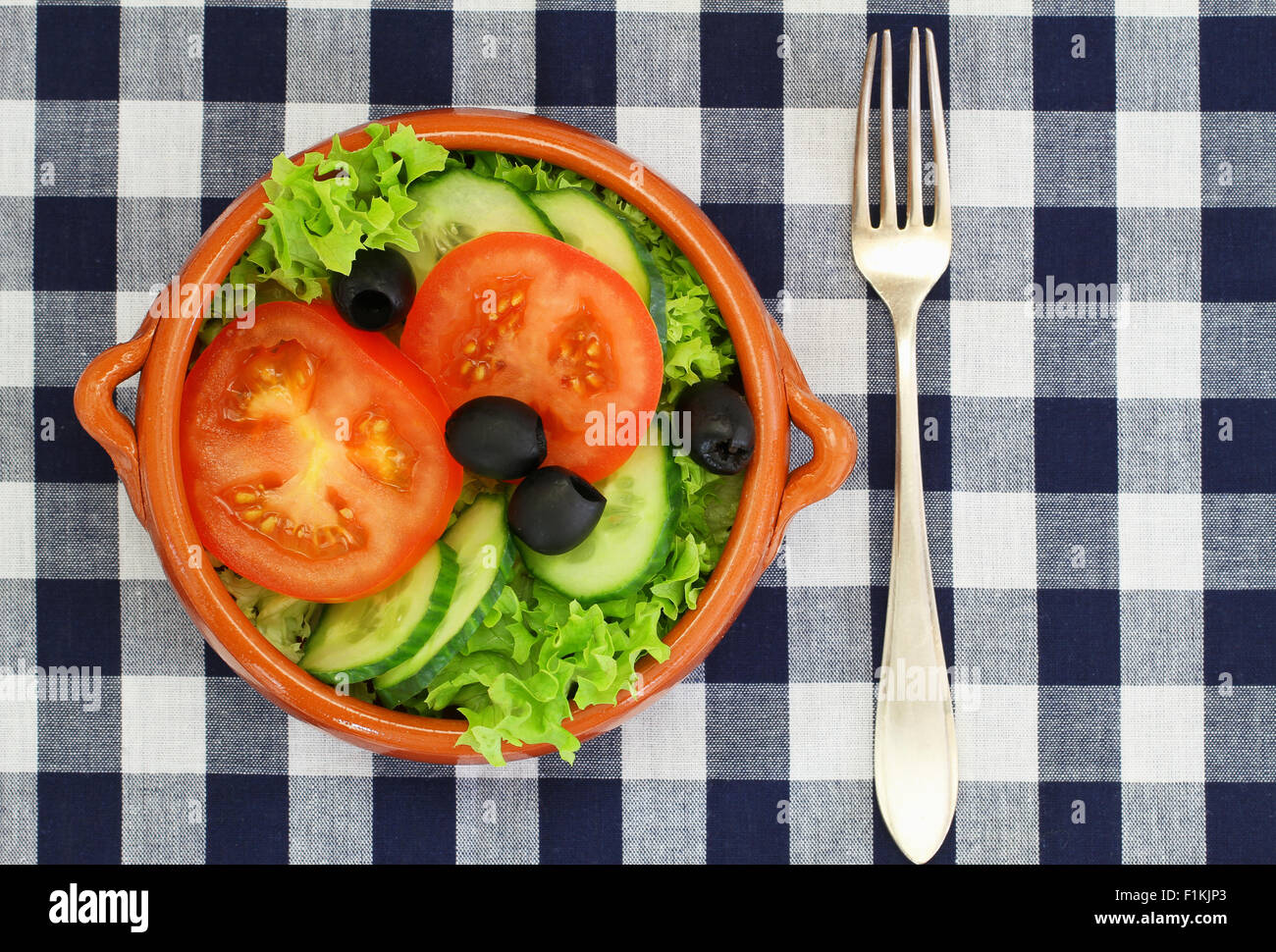 Schüssel Salat mit Kopfsalat, Tomaten, Gurken und schwarzen Oliven auf kariertem Stoff Stockfoto