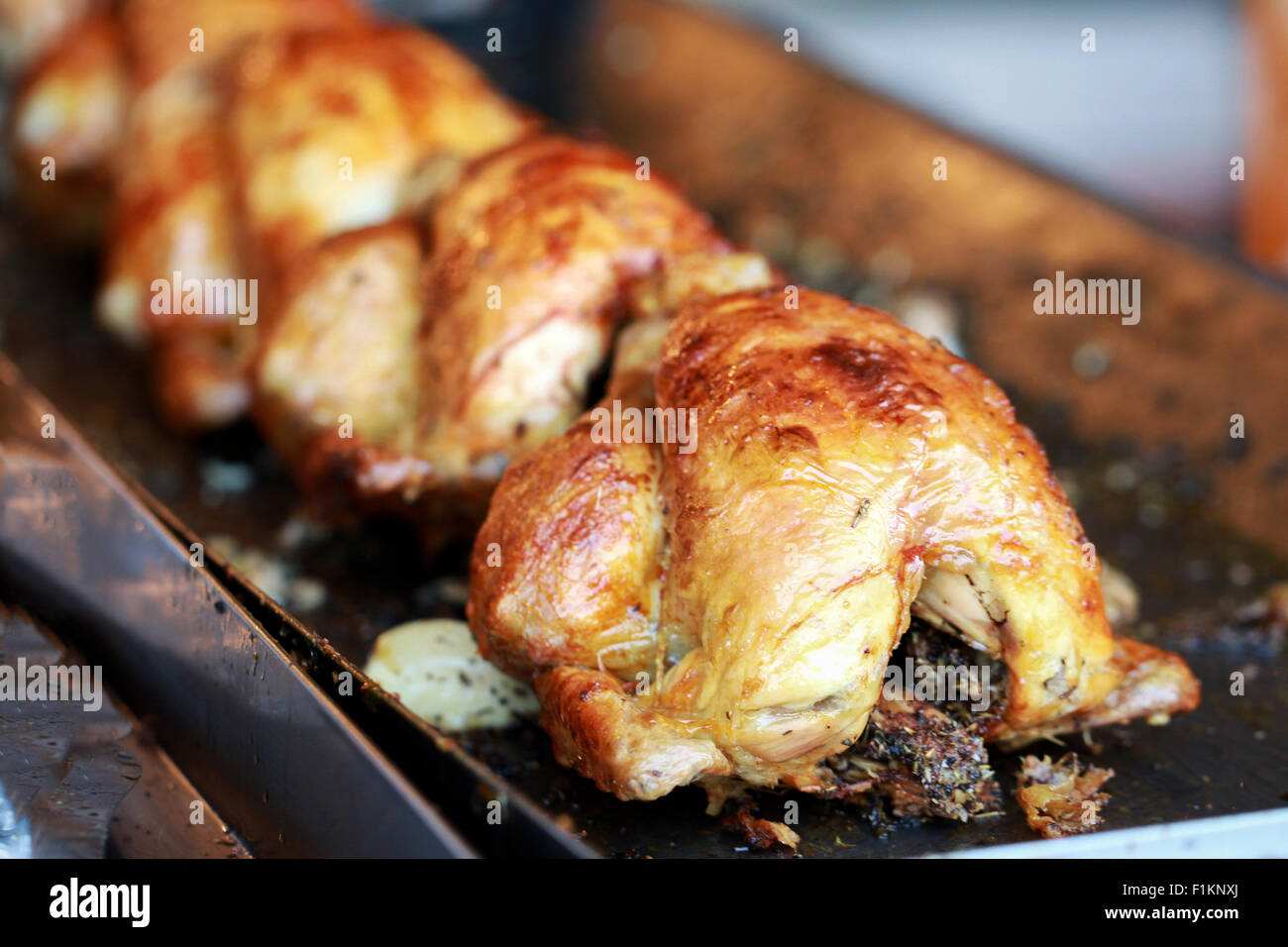 Eine Reihe von frisch gekocht, am Spieß gebratene Hühner, auf einem Tablett zum Kauf bereit. Sie haben eine goldene knusprige Haut und sind gefüllt mit Knoblauch und Kräutern Stockfoto