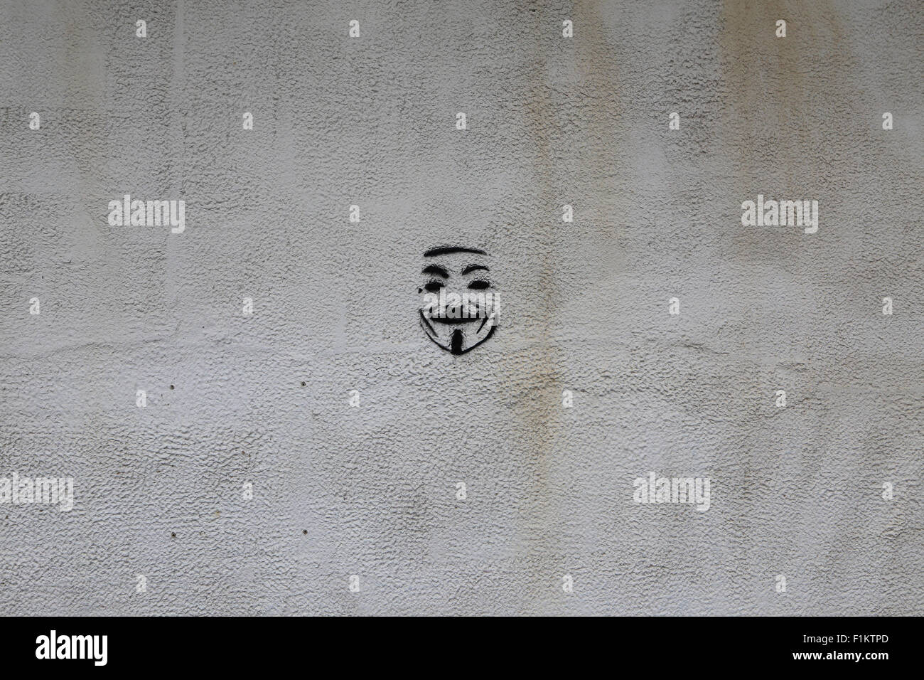 Eine isolierte "Anonymous" Guy Fawkes Schablone Kunst auf eine schlichte weiße Wand. Stockfoto