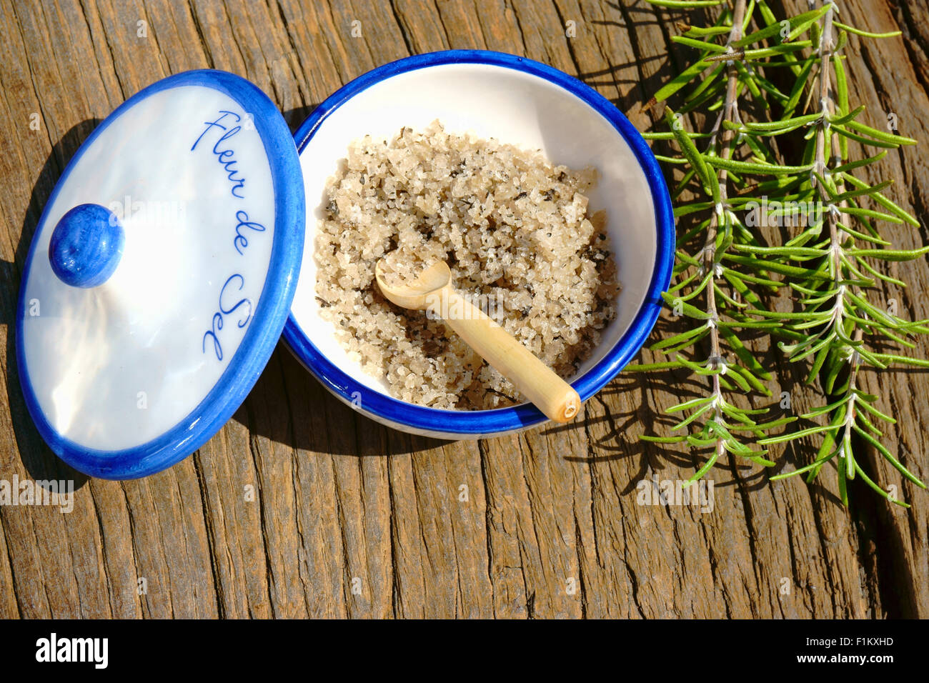Kleine Porzellanschale mit Fleur de Sel und einem Zweig Rosmarin auf einem rustikalen Holztisch Stockfoto