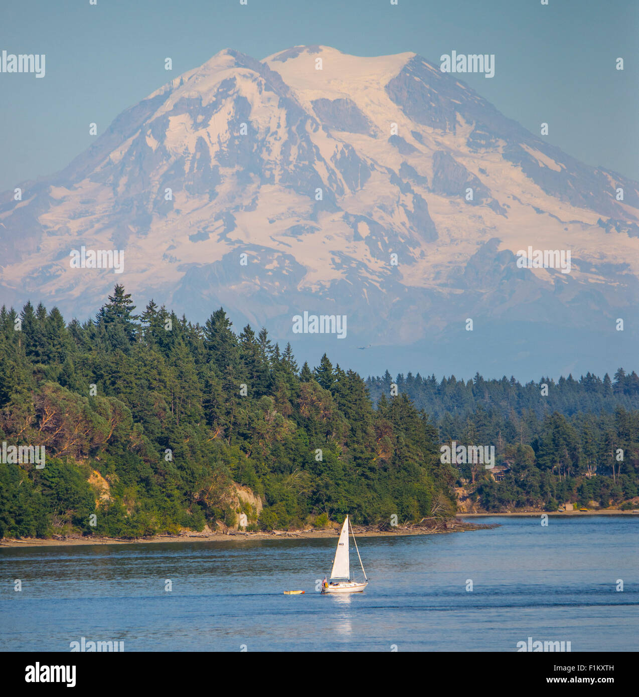 Landschaftlich reizvolle Nahaufnahme des Mount Rainier mit Menschen, die ein Segelboot segeln. Puget Sound, Squaxin Island, US-Bundesstaat Washington. Stockfoto