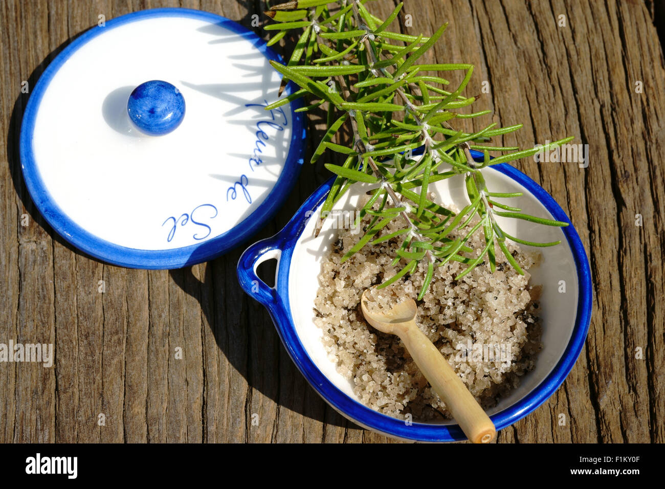 Kleine Porzellanschale mit Fleur de Sel und einem Zweig Rosmarin auf einem rustikalen Holztisch Stockfoto