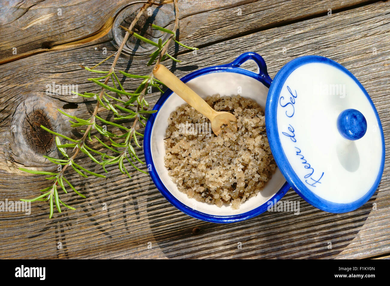 Kleine Porzellanschale mit Fleur de Sel und einem Zweig Rosmarin auf einem rustikalen Holztisch Stockfoto