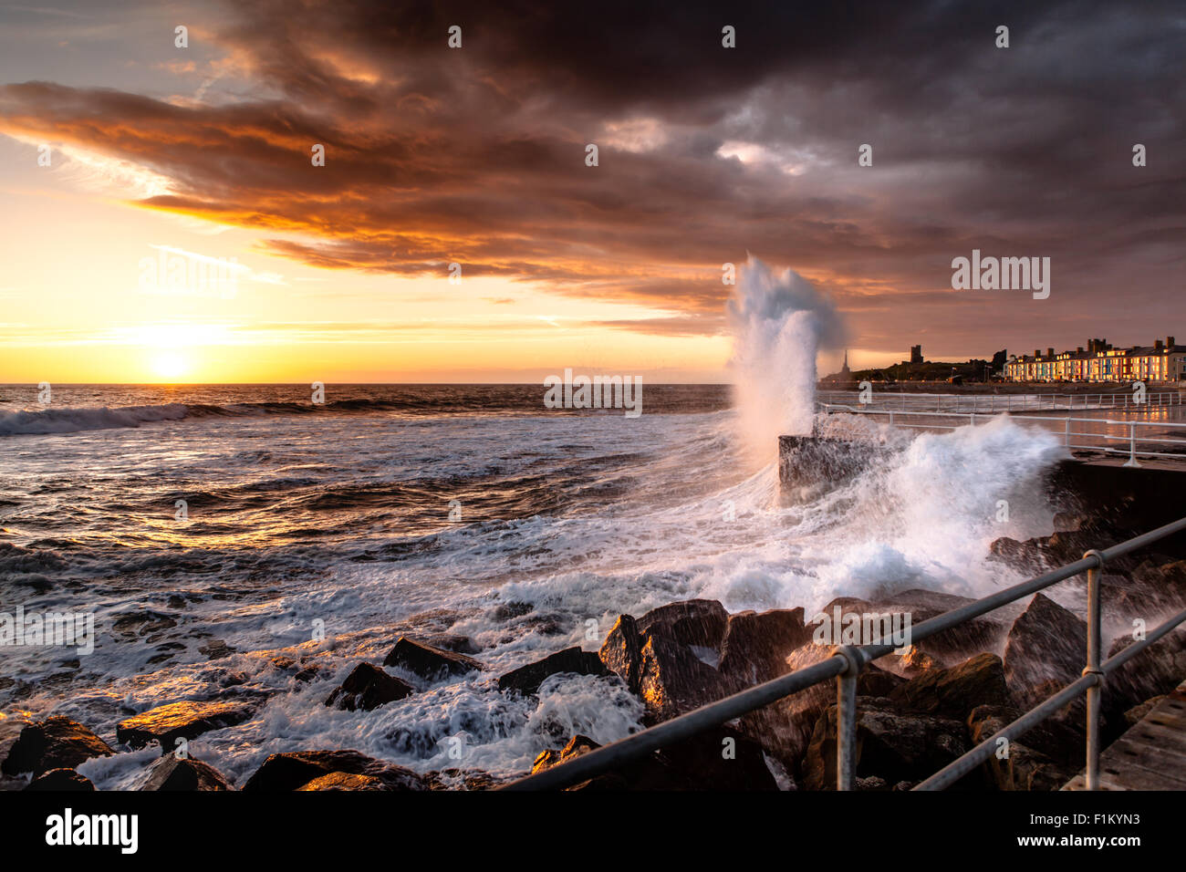 Sonnenuntergang an der Küste von Aberystwyth mit den Wellen brechen an der Hafen-Wand mit einem dunklen Stimmungsvoller Himmel kommen quer durch die Stadt Stockfoto