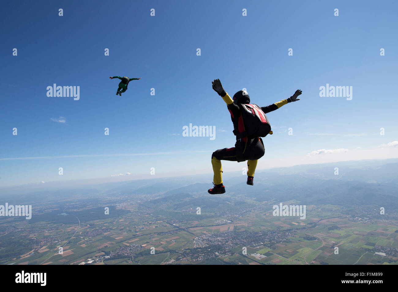 Diese Freefly-Fallschirmspringer fliegen hoch in den blauen Himmel über schöne Landschaft. Dabei fliegen sie training sitzen die Position. Stockfoto