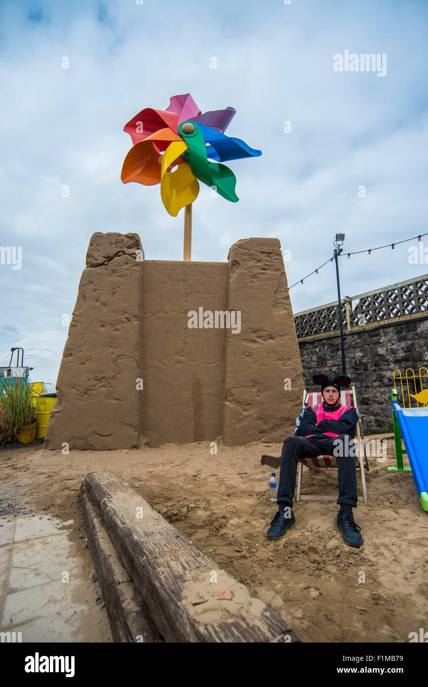 Angestellter bei Banksy Dismaland Verblüffung Park sitzt auf einer gefälschten Strand vor eine enorme Sandburg. Stockfoto