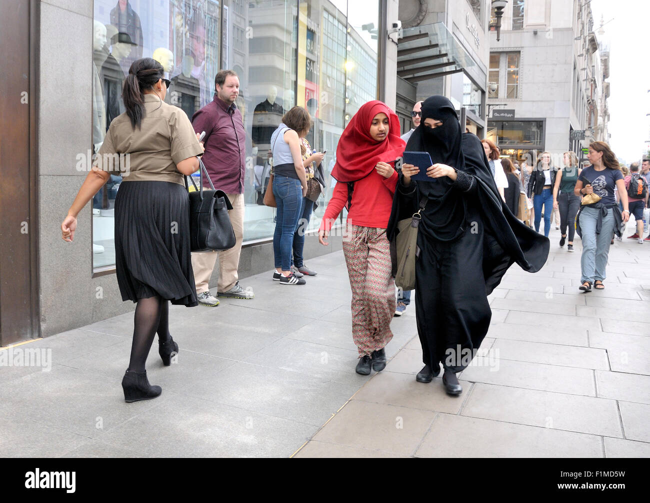 London, England, Vereinigtes Königreich. Zwei junge muslimische Frauen zu Fuß und mit Blick auf ein iPhone Stockfoto