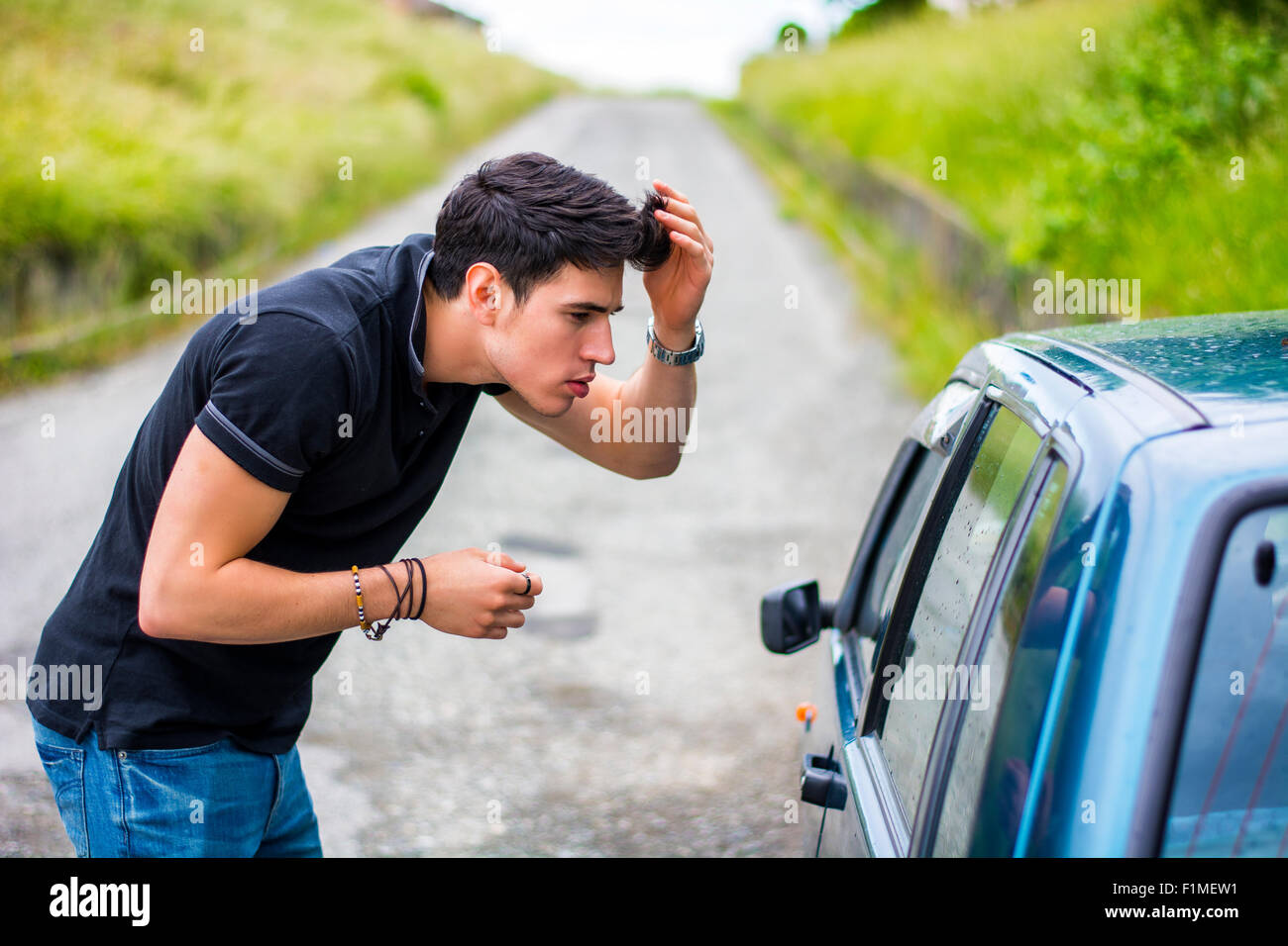Eine halbe Stelle erschossen ein hübscher Junge Mann betrachten seine Reflexion über ein Autofenster und Befestigung sein Haar. Stockfoto