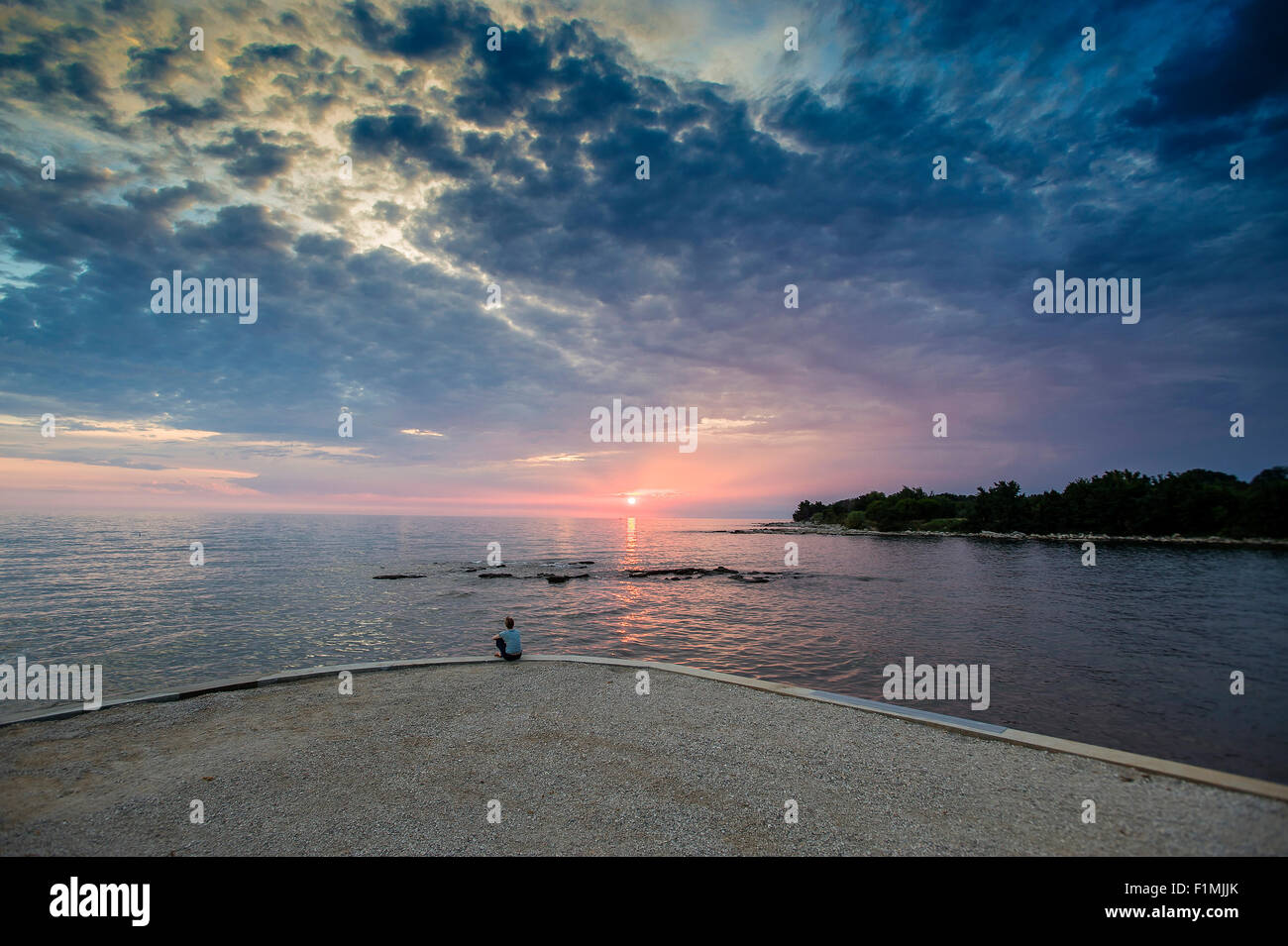 Frau sitzt und Sonnenuntergang am Ufer des Meeres Stockfoto