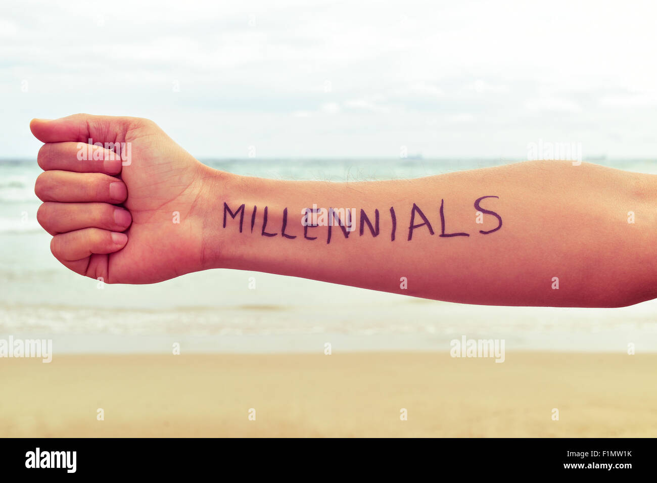Nahaufnahme eines jungen Mannes mit dem Wort Millennials geschrieben in seinem Arm direkt am Meer Stockfoto