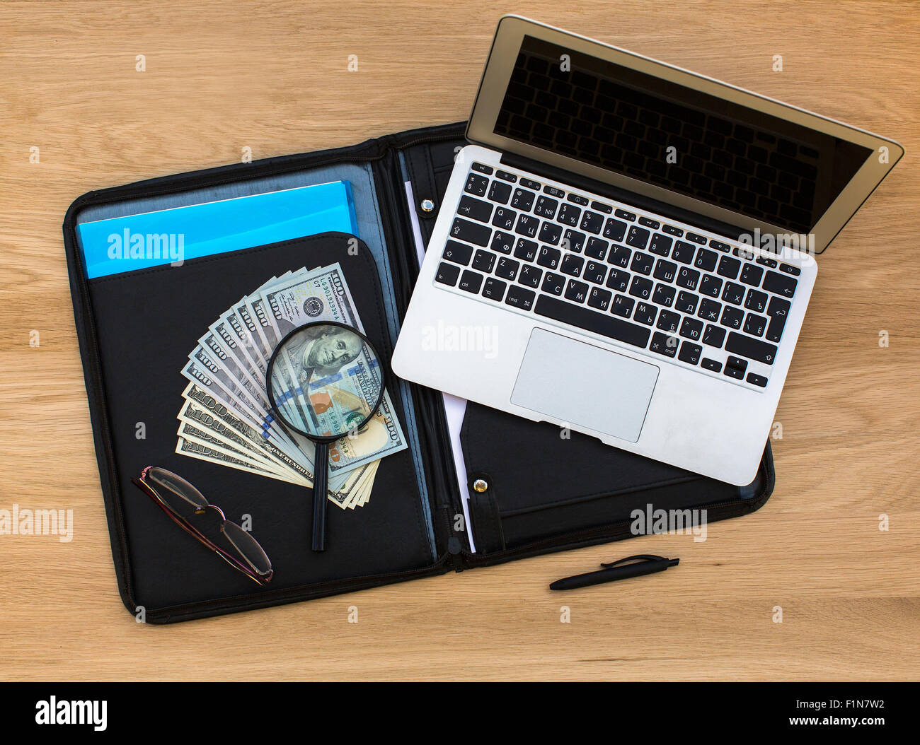 US-hundert-Dollar-Scheine unter Lupe auf Business-Ordner und Laptop auf Eiche Holz Textur, Ansicht von oben liegen. Stockfoto