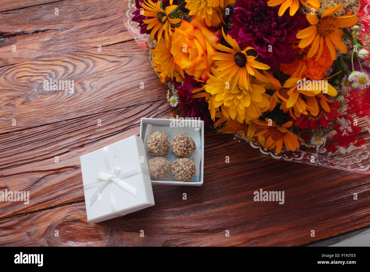 auf einem Holzbrett sind, einen Blumenstrauß und eine Schachtel Pralinen Stockfoto