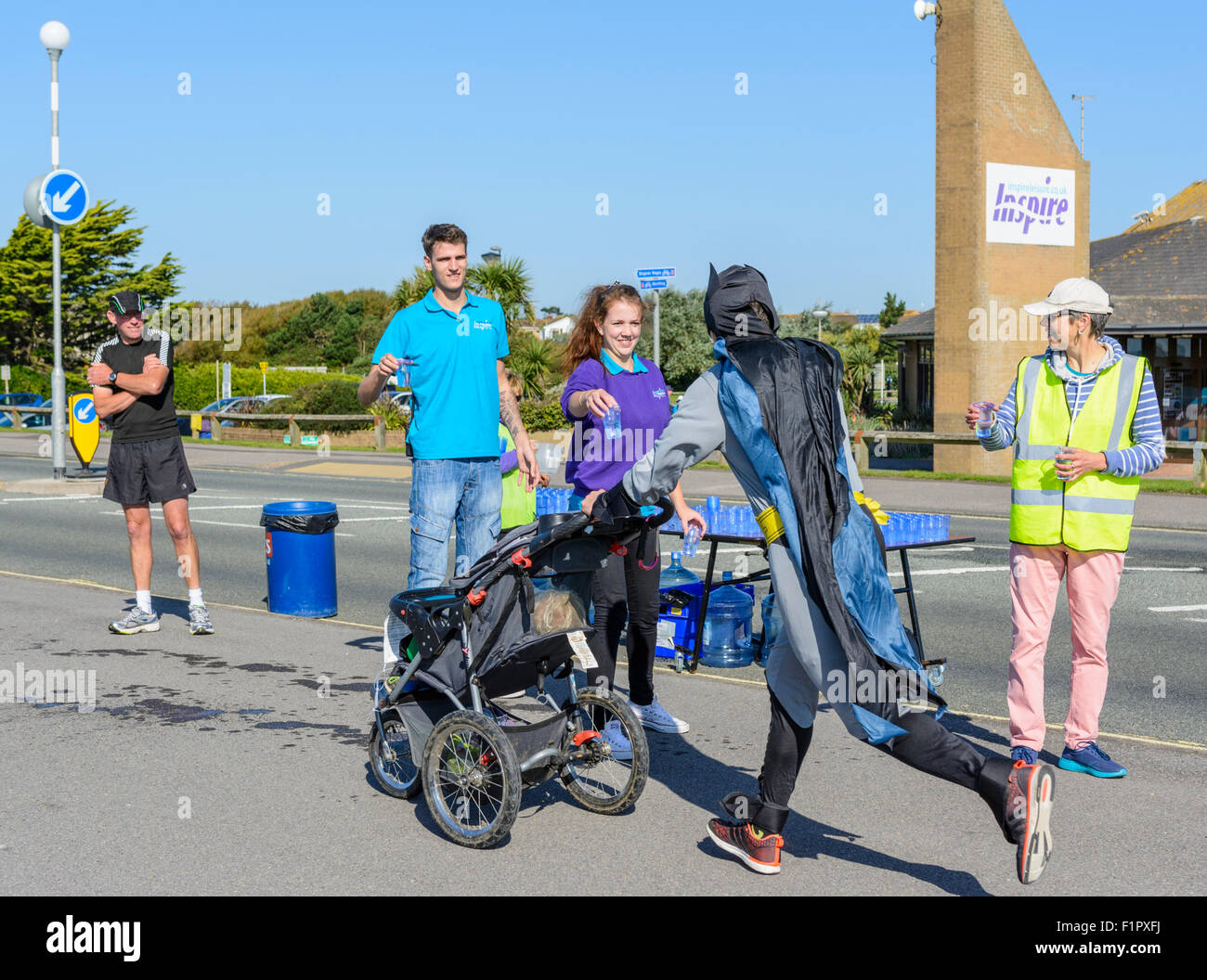 Liebe runner gekleidet an Batman und Nehmen auf Wasser bei einer Station, an der Kastanie Haus 10 k Spendenlauf in Littlehampton, West Sussex, England, UK. Stockfoto