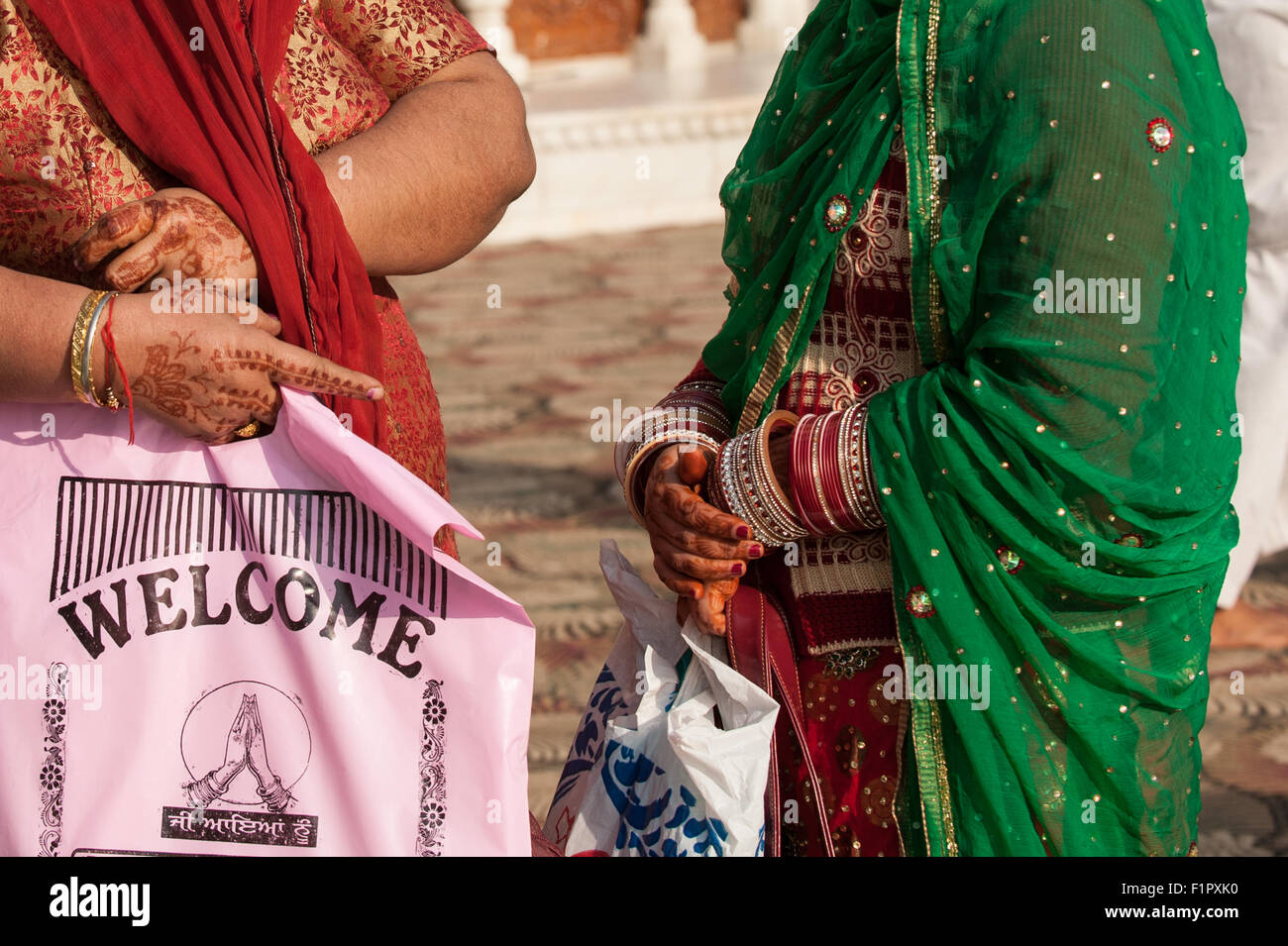 Amritsar, Punjab, Indien. Zwei Frauen, ihre Hände mit Henna komplizierten Mustern bemalt. Man hält eine rosa Plastiktüte mit "Willkommen" Englisch und Punjabi schriftlich. Stockfoto