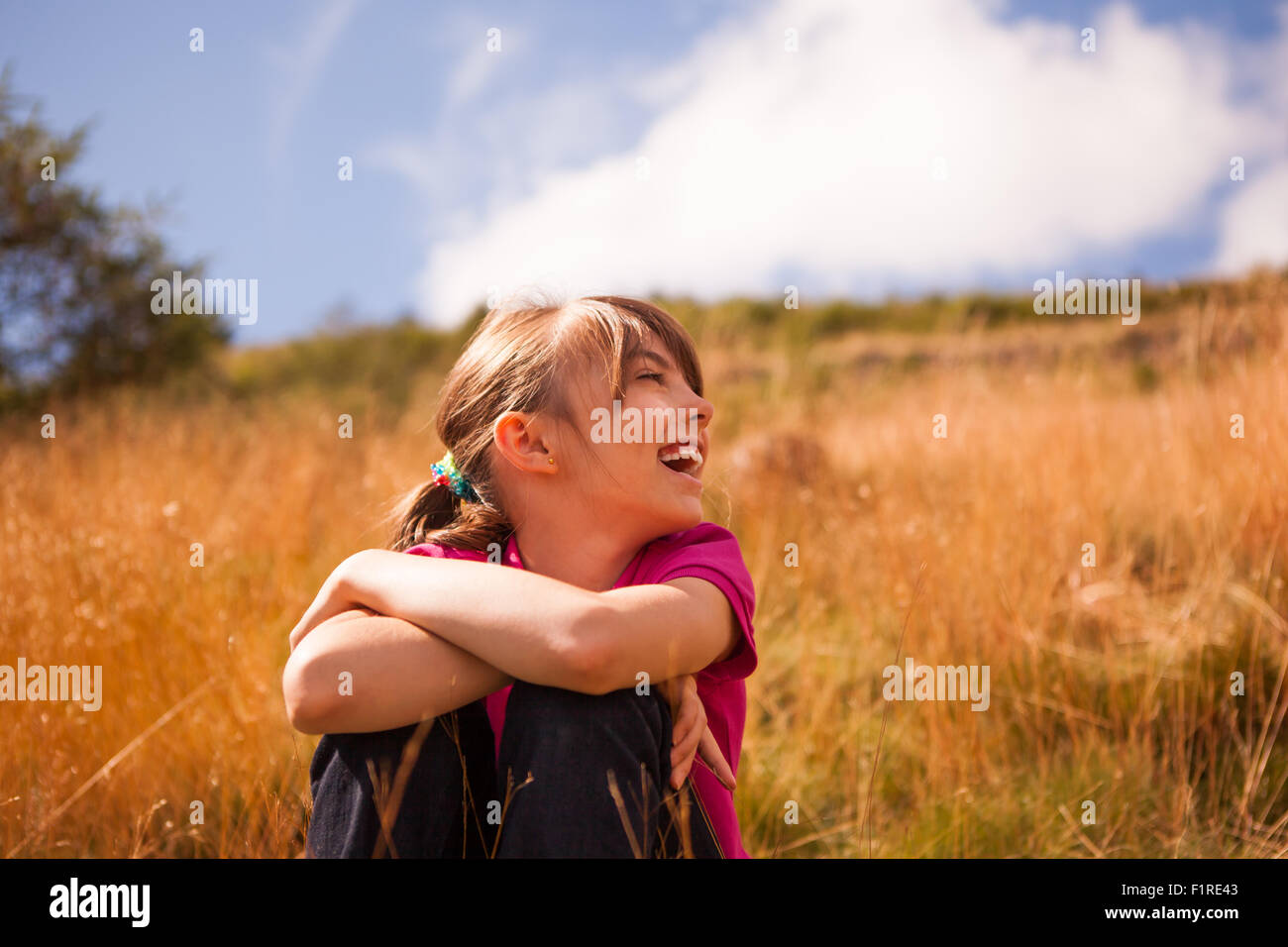 Hübsches junges Mädchen sitzt auf einem Rasen Ufer an einem hellen Tag lachen Stockfoto