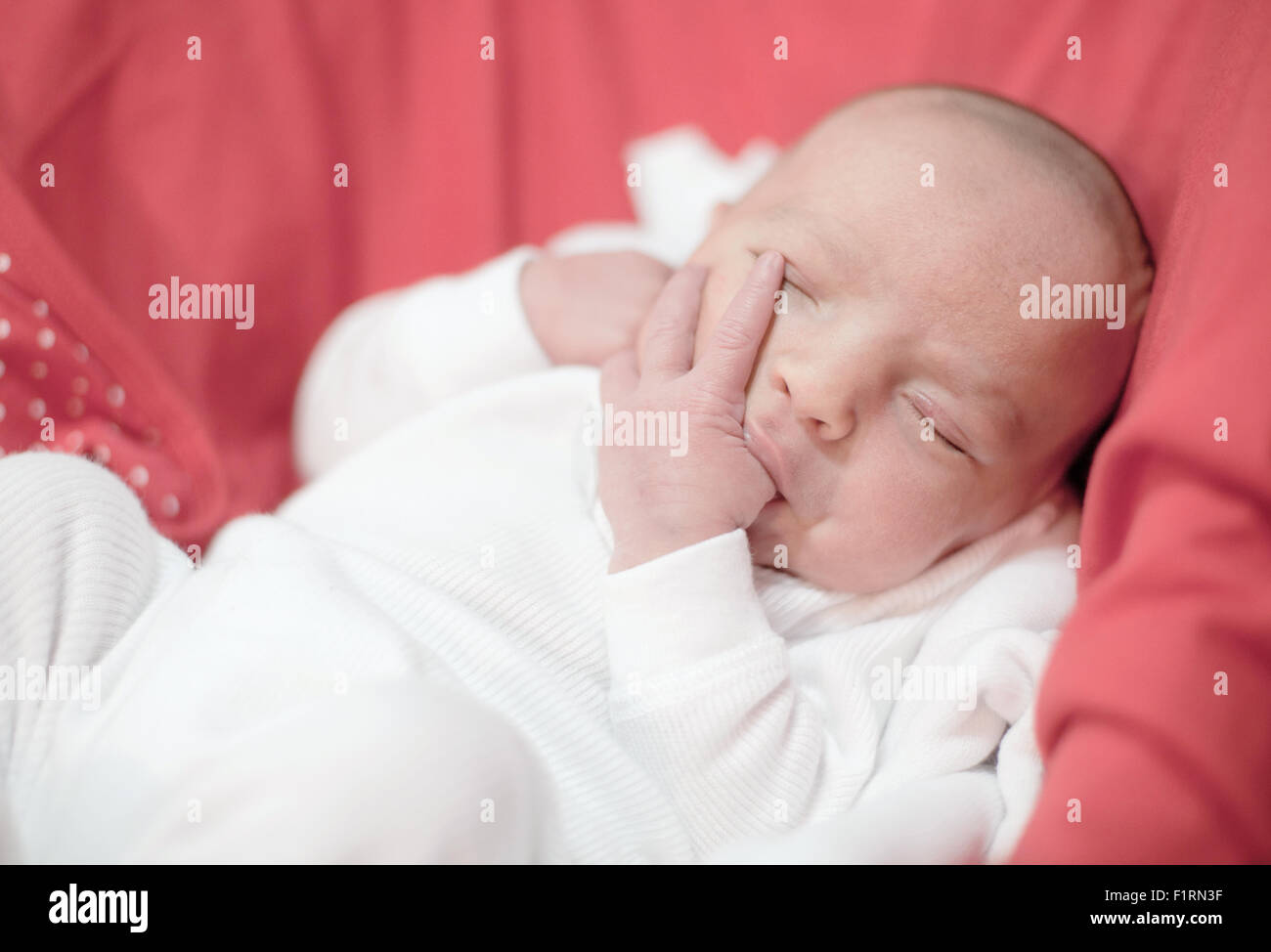 Niedlichen neugeborenen Mädchen schläft mit Finger im Mund Stockfoto