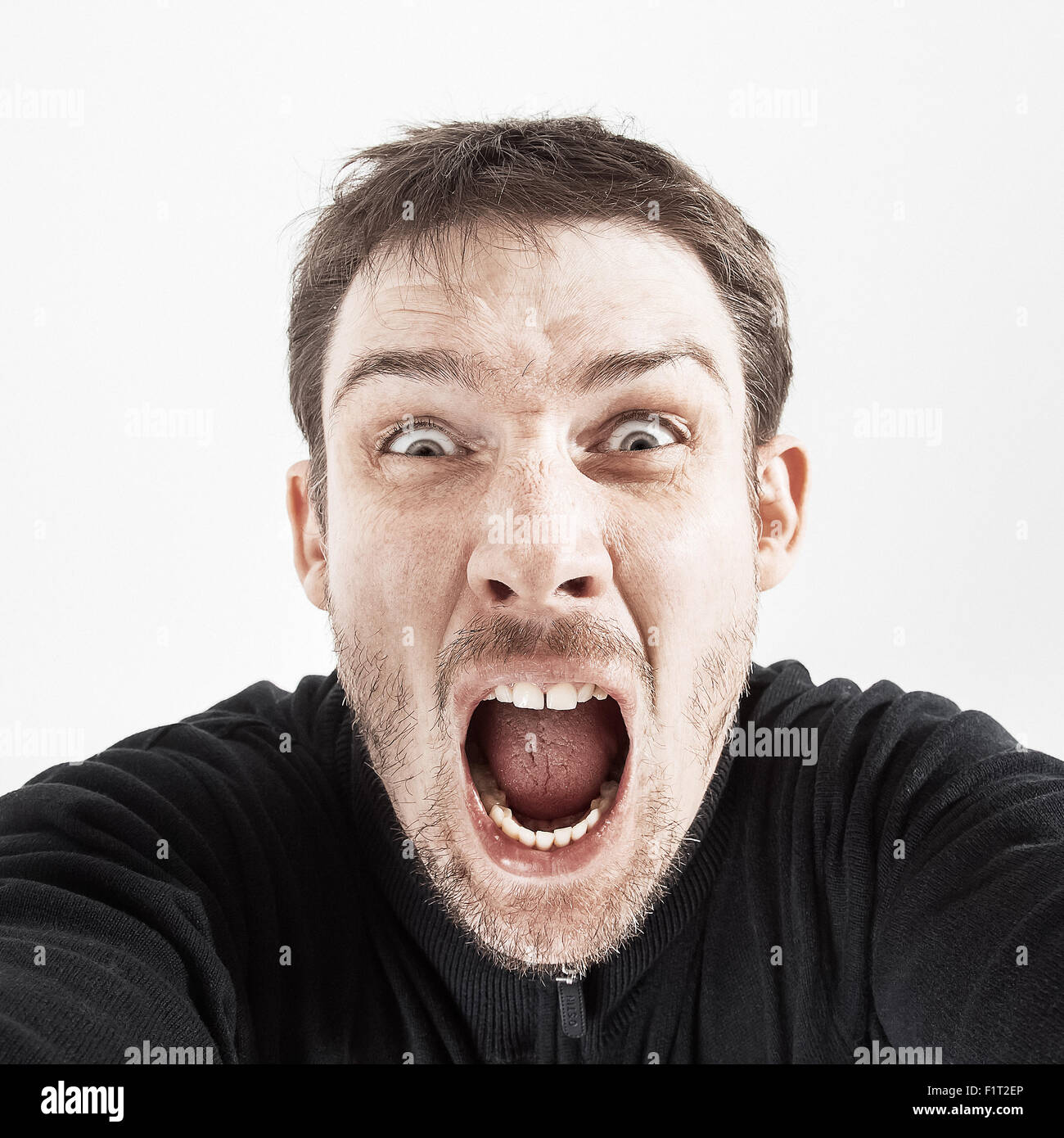 unrasiert Mann in einer schwarzen Jacke auf einem weißen Hintergrund schreit. Stockfoto