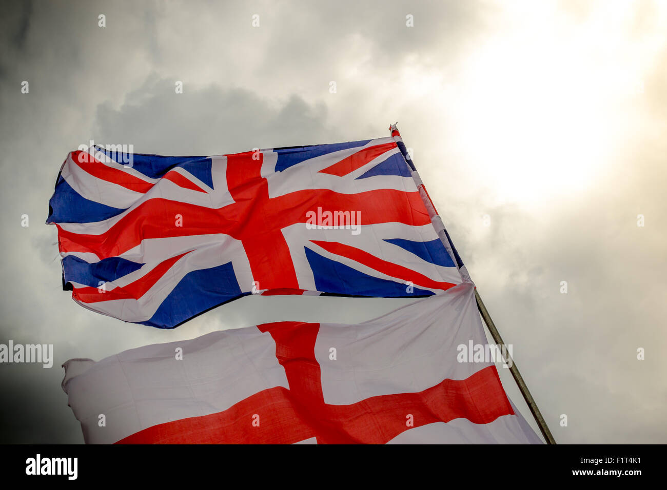 Englische Union Jack und Saint George Flagge im Wind gegen grauen bewölktem Himmel Stockfoto