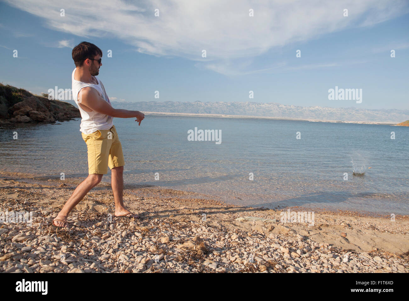 Junger Mann am Strand Steinewerfen Stockfoto