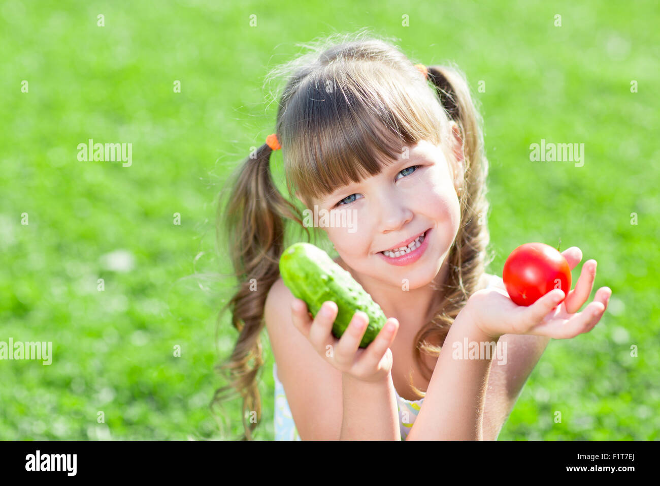 Glückliches kleines Mädchen sitzen auf dem Rasen mit Gemüse am Tageszeit. Konzept von gesunden Lebensmitteln. Stockfoto