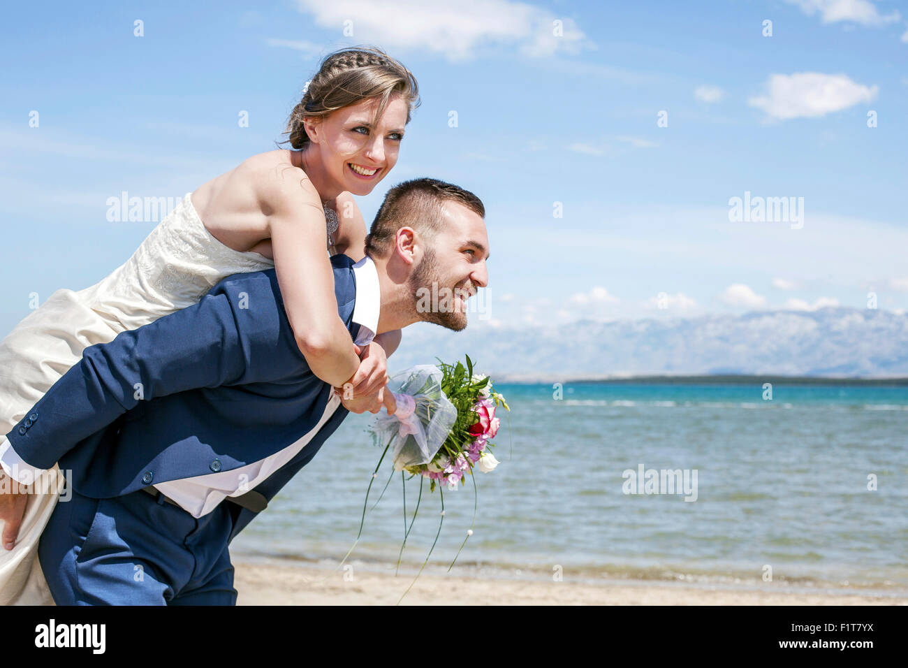 Bräutigam und Braut Huckepack Reiten am Strand Stockfoto