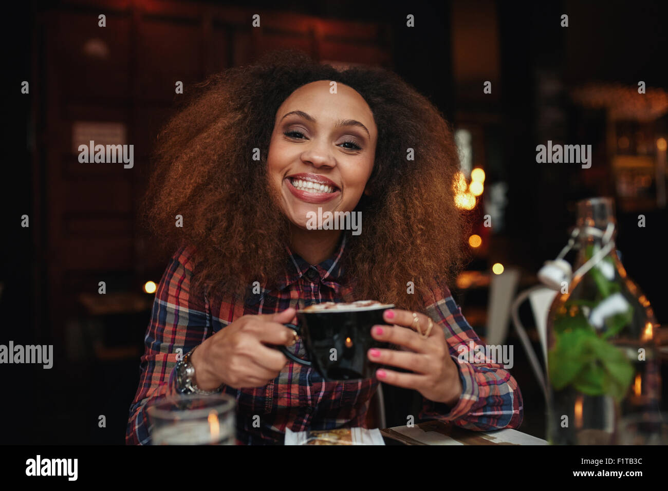 Porträt der jungen Frau Kaffee trinken. Afrikanische Frau sitzen im Café hält eine Tasse Kaffee, Blick auf die Kamera zu Lächeln. Stockfoto