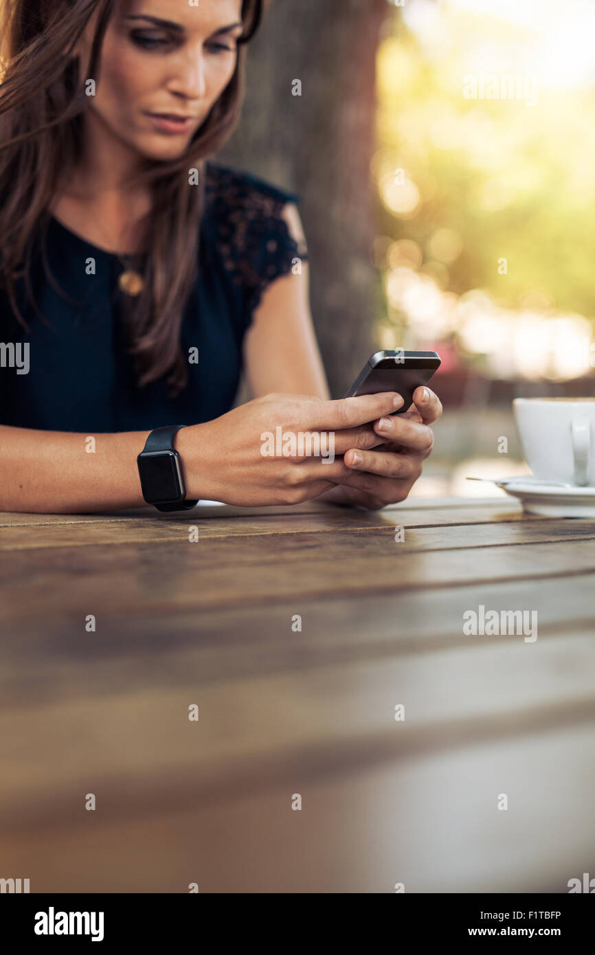 Bild der jungen weiblichen lesen eine SMS-Nachricht auf ihr Smartphone zugeschnitten. Frau mit Smartphone in ein Café im Freien. Stockfoto