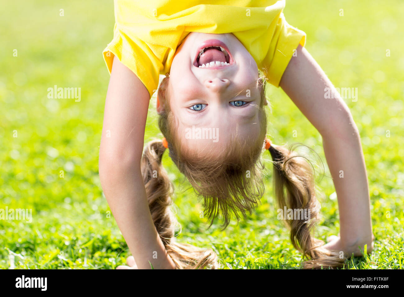Glückliches Kind hat Spaß stehen Kopf nach unten auf dem grünen Rasen Stockfoto