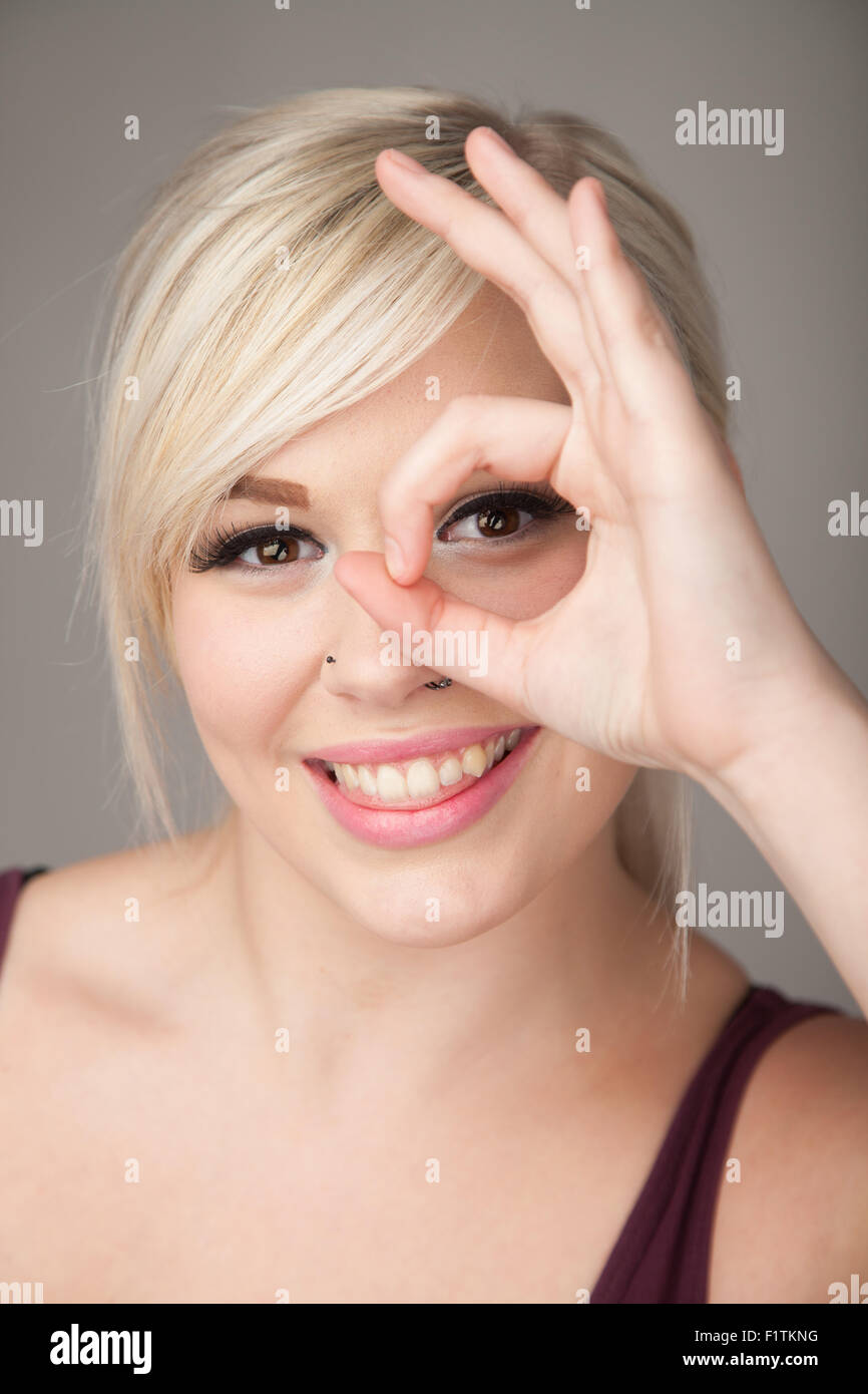 Ziemlich junges Mädchen machen ein Okay mit ihrer Hand und schaut durch den Kreis von ihm signieren. Stockfoto