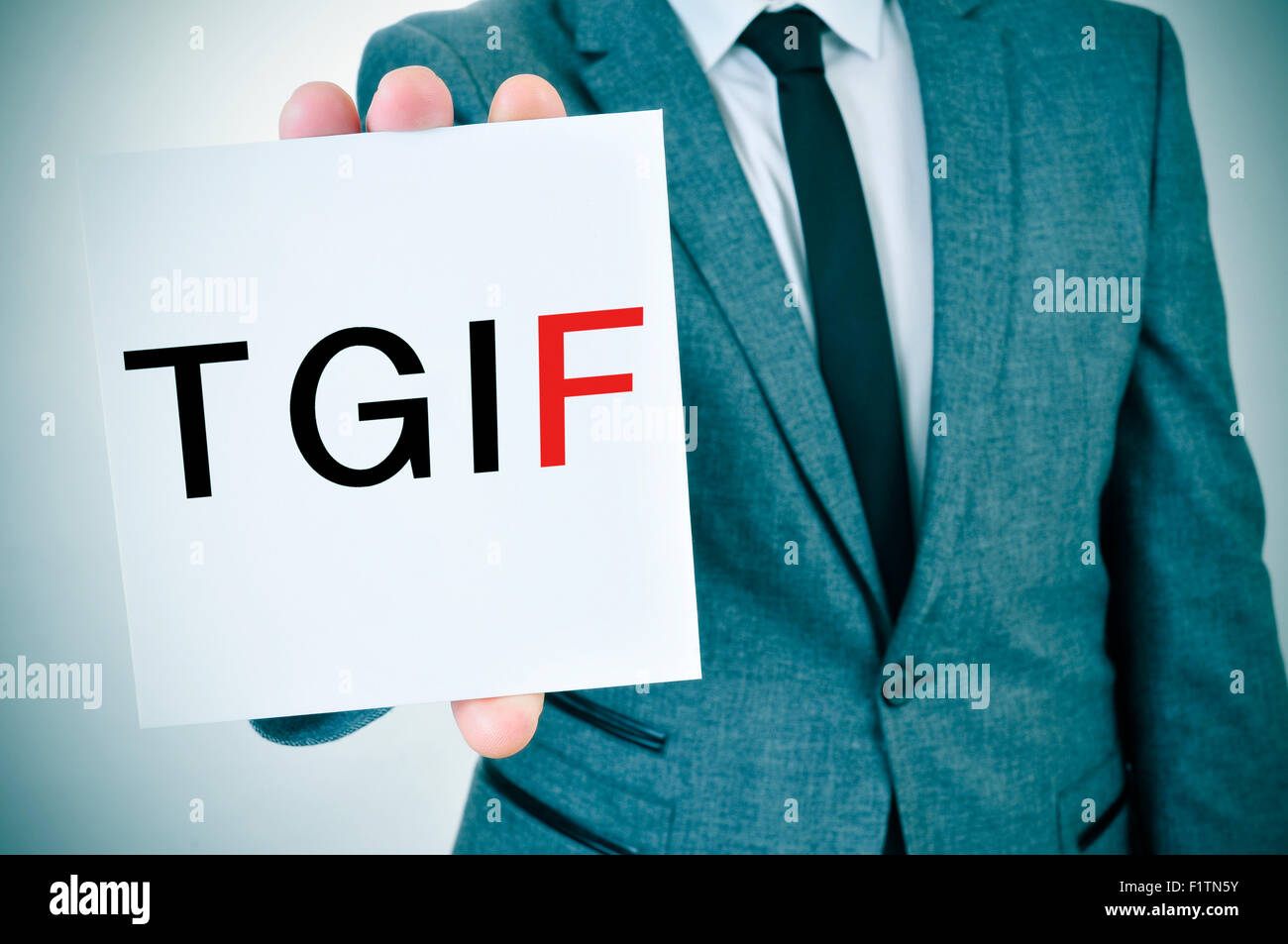 ein junger Mann im Anzug zeigt ein Schild mit dem Wort TGIF, danke Gott es ist Freitag, geschrieben Stockfoto