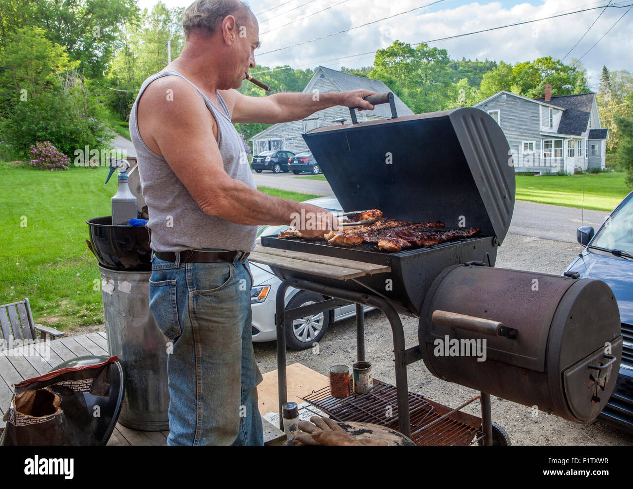 Ein Mann raucht eine Zigarre und Grillen Huhn auf einem Holzkohlegrill. Stockfoto