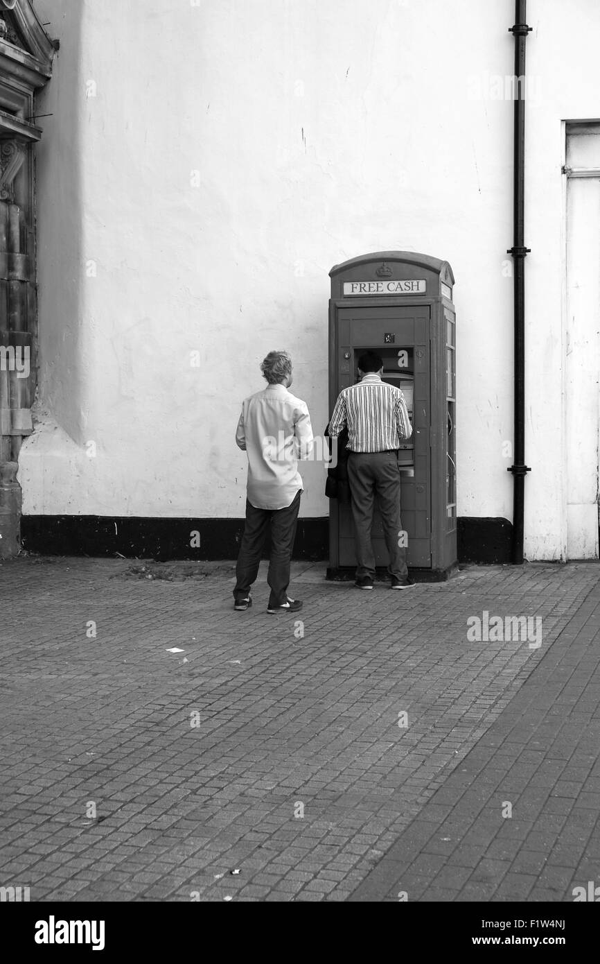 Zwei Männer, die Warteschlangen an einem Geldautomaten Bargeld darauf Maschine in eine alte alte traditionelle Telefonzelle. September 2015 Stockfoto