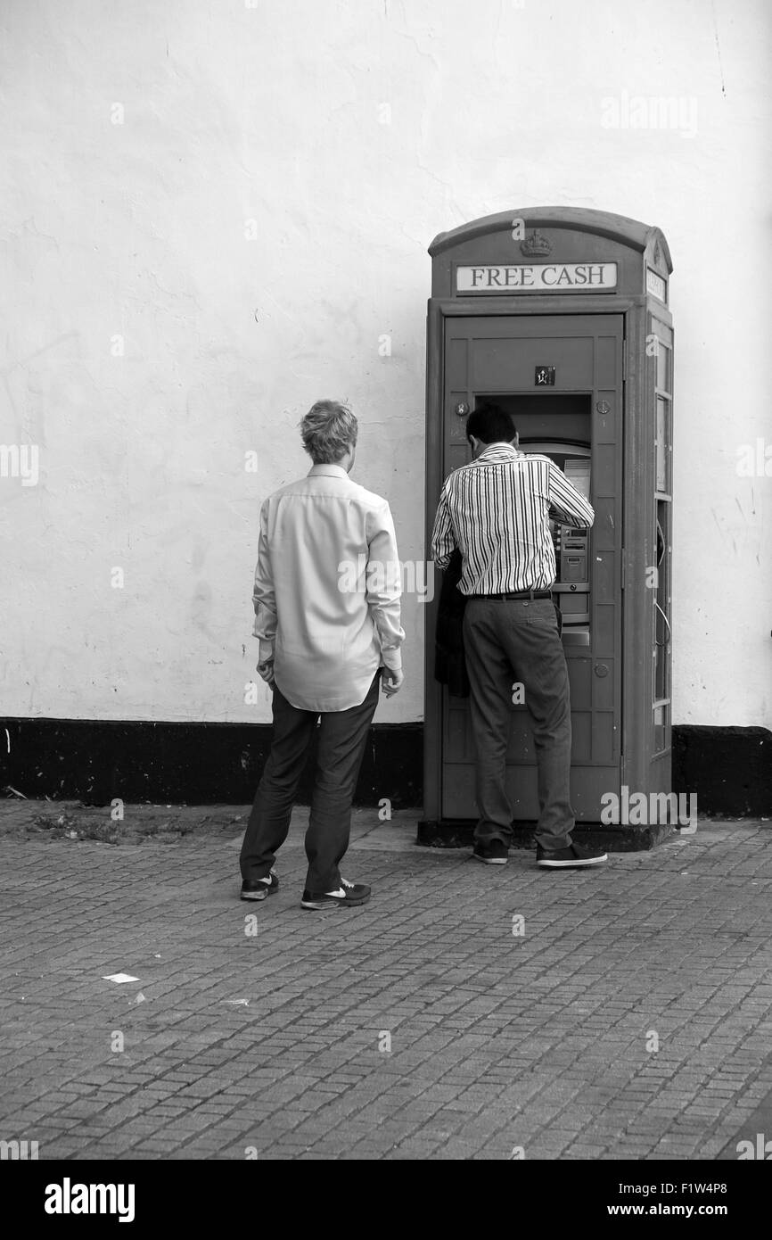 Zwei Männer, die Warteschlangen an einem Geldautomaten Bargeld darauf Maschine in eine alte alte traditionelle Telefonzelle. September 2015 Stockfoto