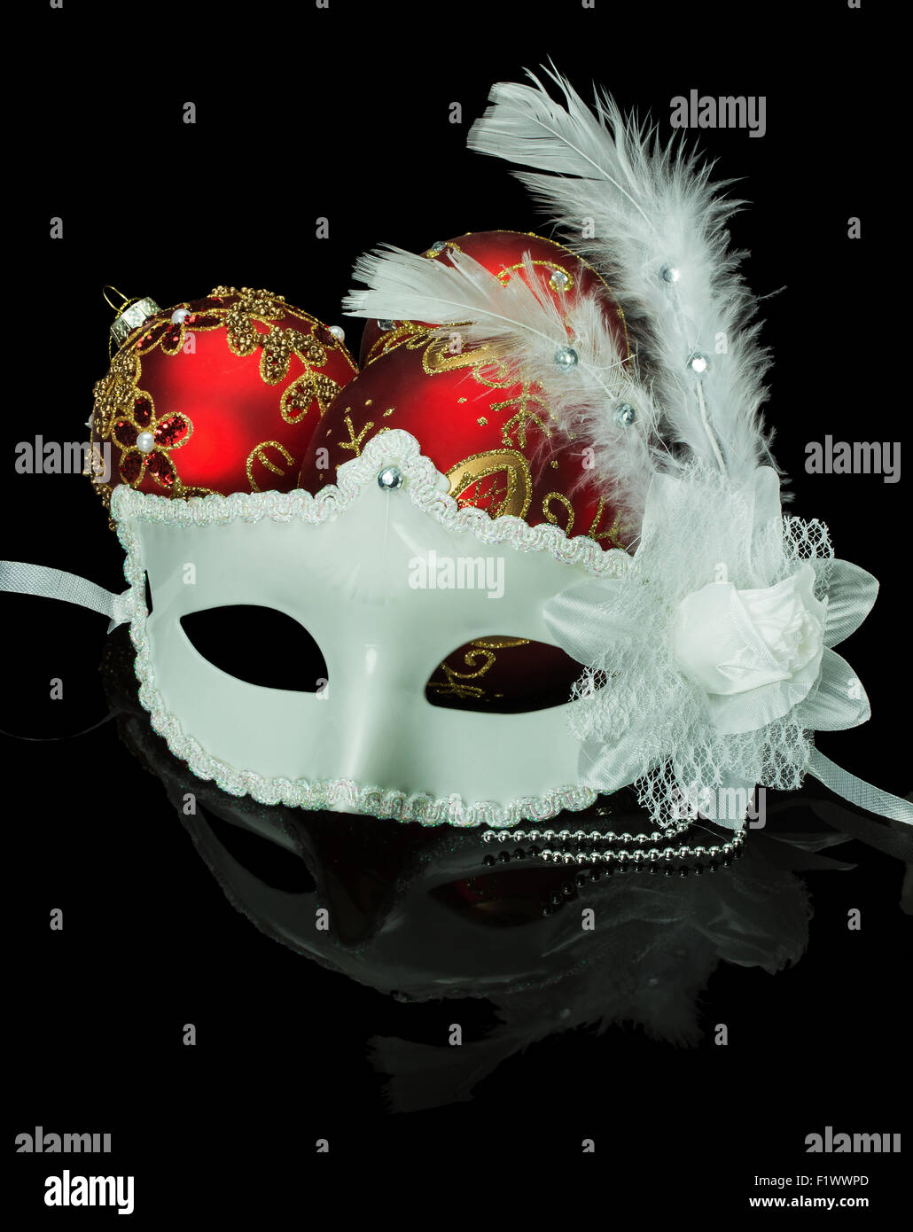 Weiße Maske und Weihnachten rote Kugeln auf einem schwarzen Hintergrund. Stockfoto